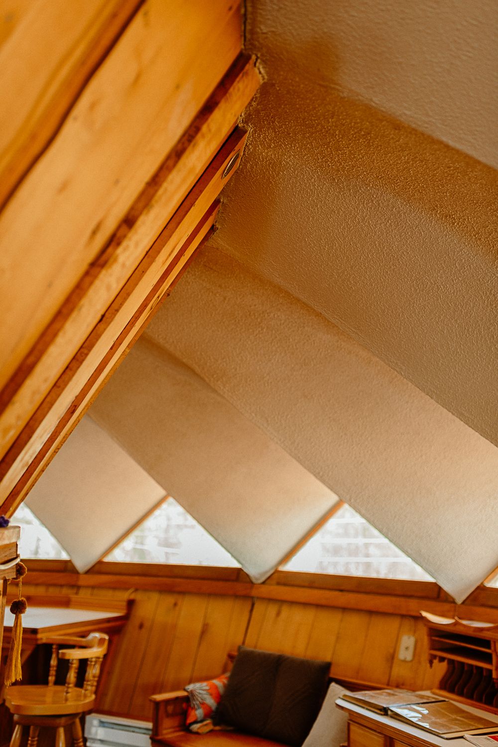 Rustic A-frame cabin interior with warm wood paneling, angled ceiling, and natural light casting geometric shadows.