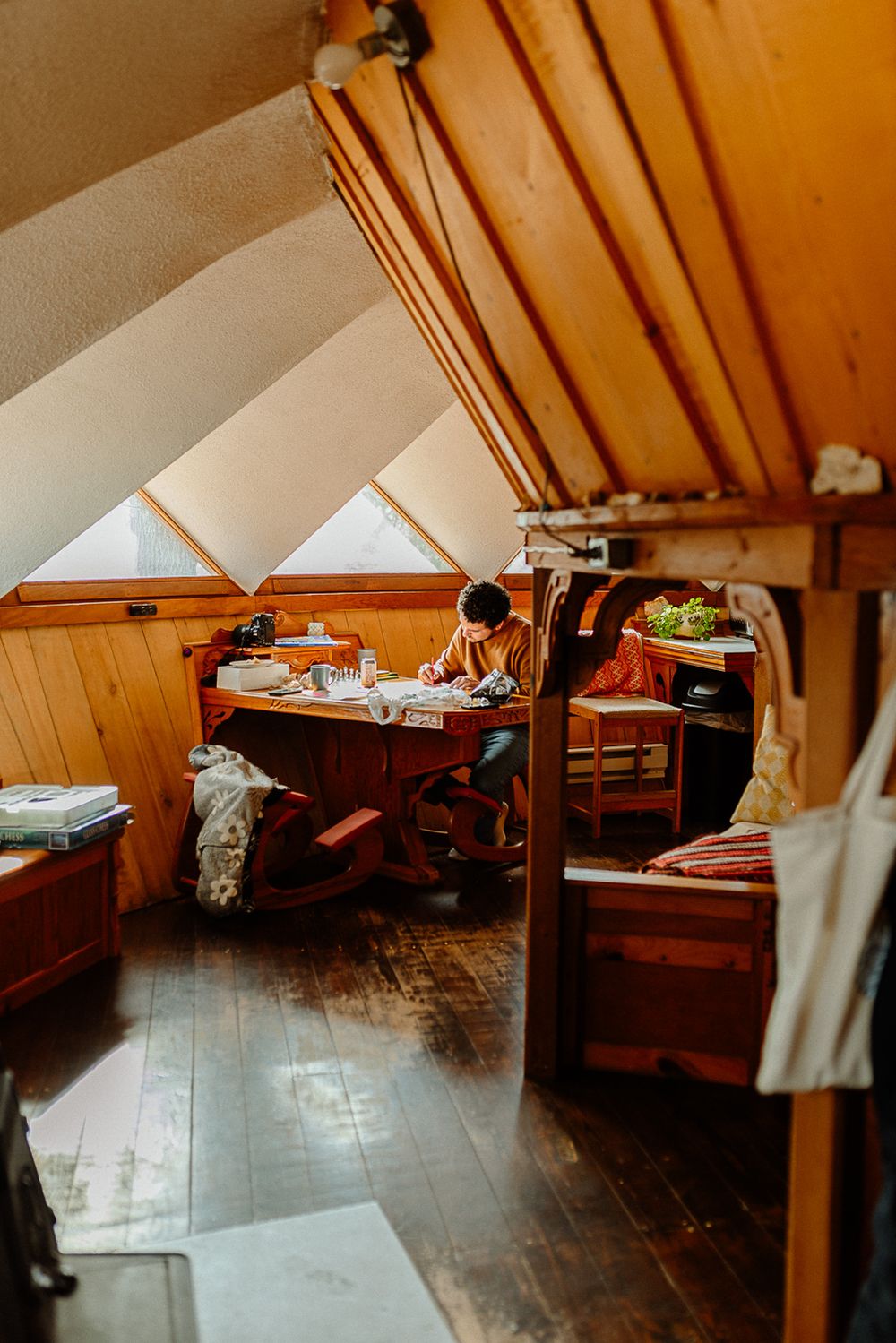 Cozy wooden attic workspace with arched ceiling, hardwood floors, and a person working at a rustic desk.