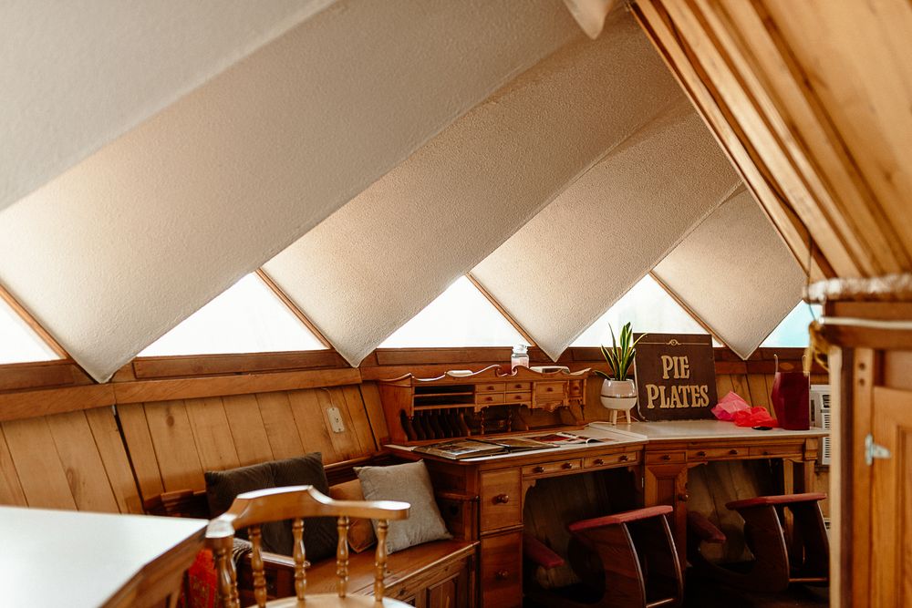 Rustic attic shop interior with slanted wooden ceiling, natural light windows, and a Pie Plates sign among vintage decor.