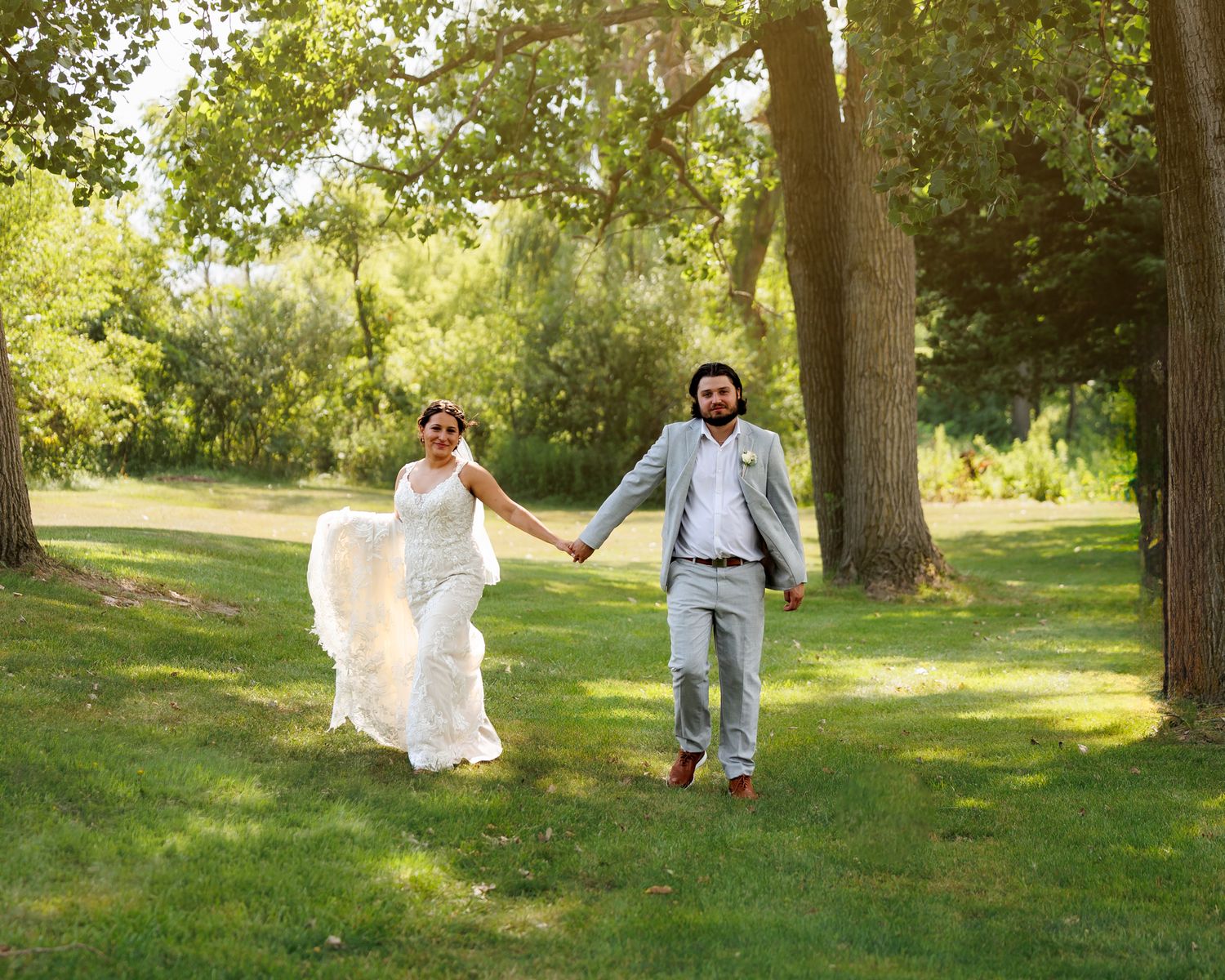 Bride and groom holding hands walking through a lush green park on their wedding day.