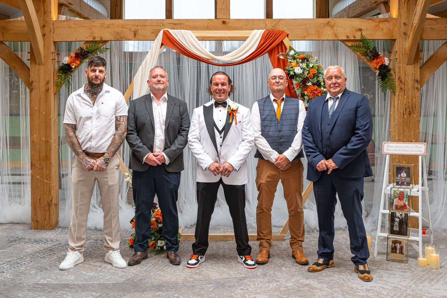 Groomsmen posing together at a wedding ceremony venue decorated with fall florals and warm autumn colors.