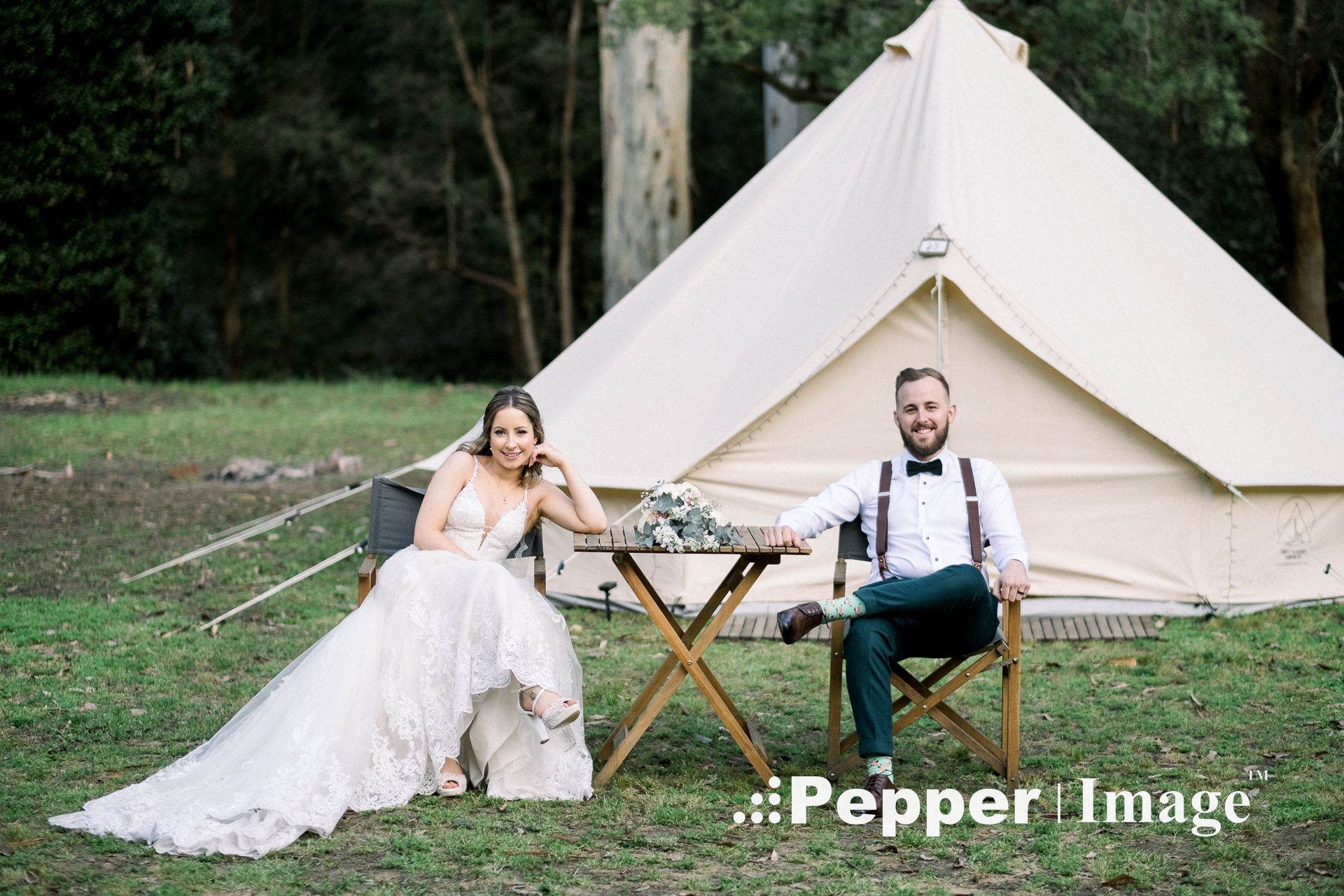 Bride and groom sit relaxing in chairs outside a glamping bell tent at their outdoor wedding.