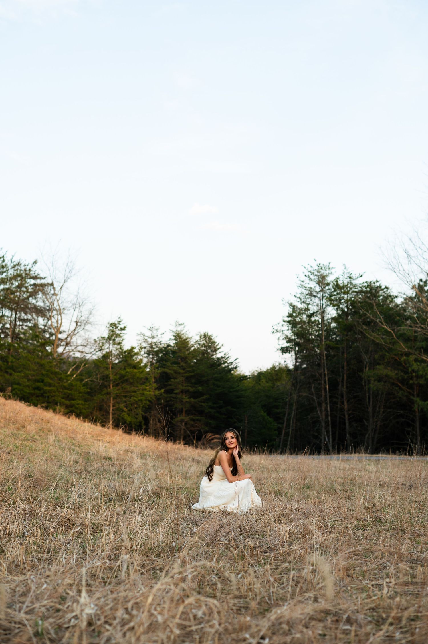 Couple dancing outdoors in a field during golden hour, woman in white dress being twirled by man in gray sweater.