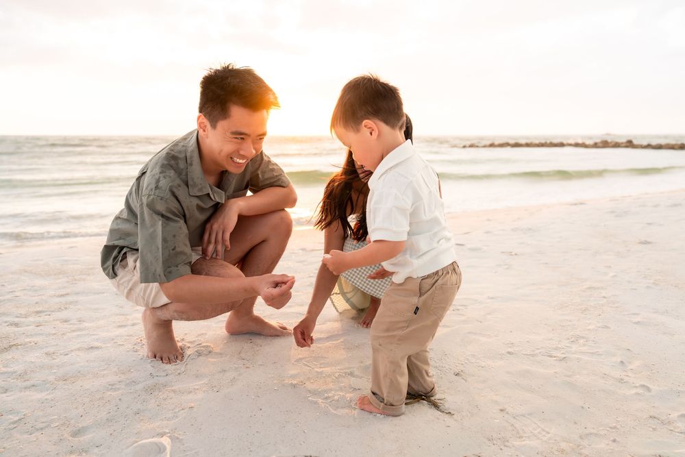 Father and toddler son playing in the sand on a sunny beach at golden hour.