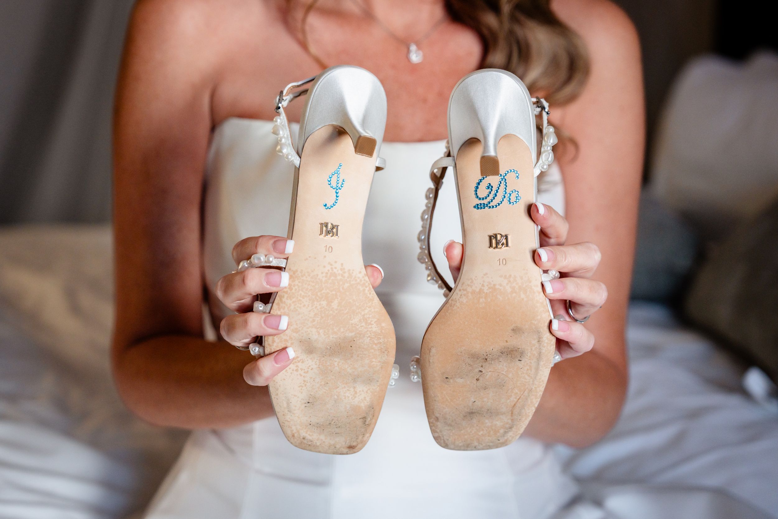 Bride holds up white wedding heels showing I Do stickers on the soles of her bridal shoes.