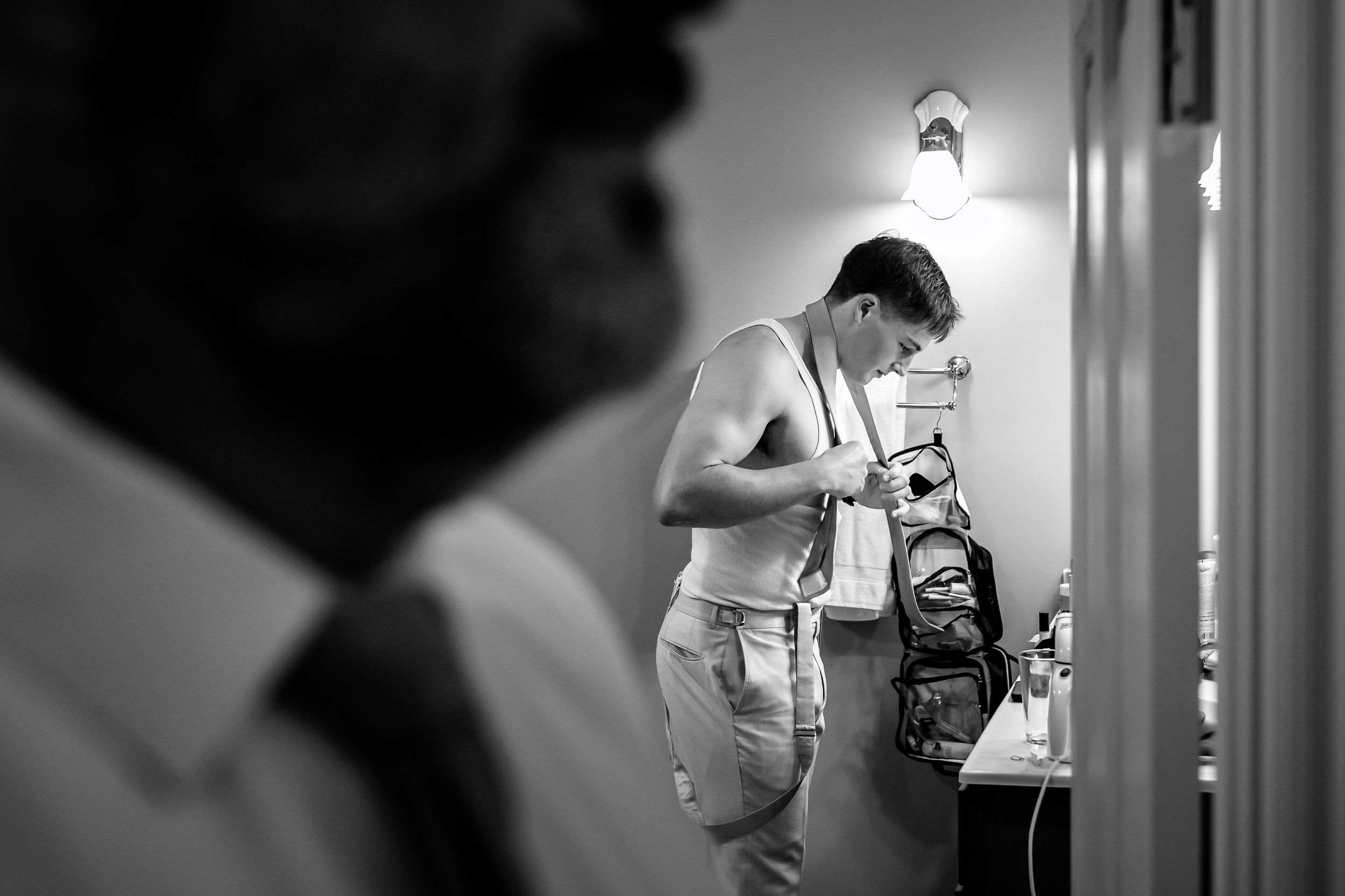 Groom getting dressed in black and white photo, adjusting his outfit while preparing for his wedding day.