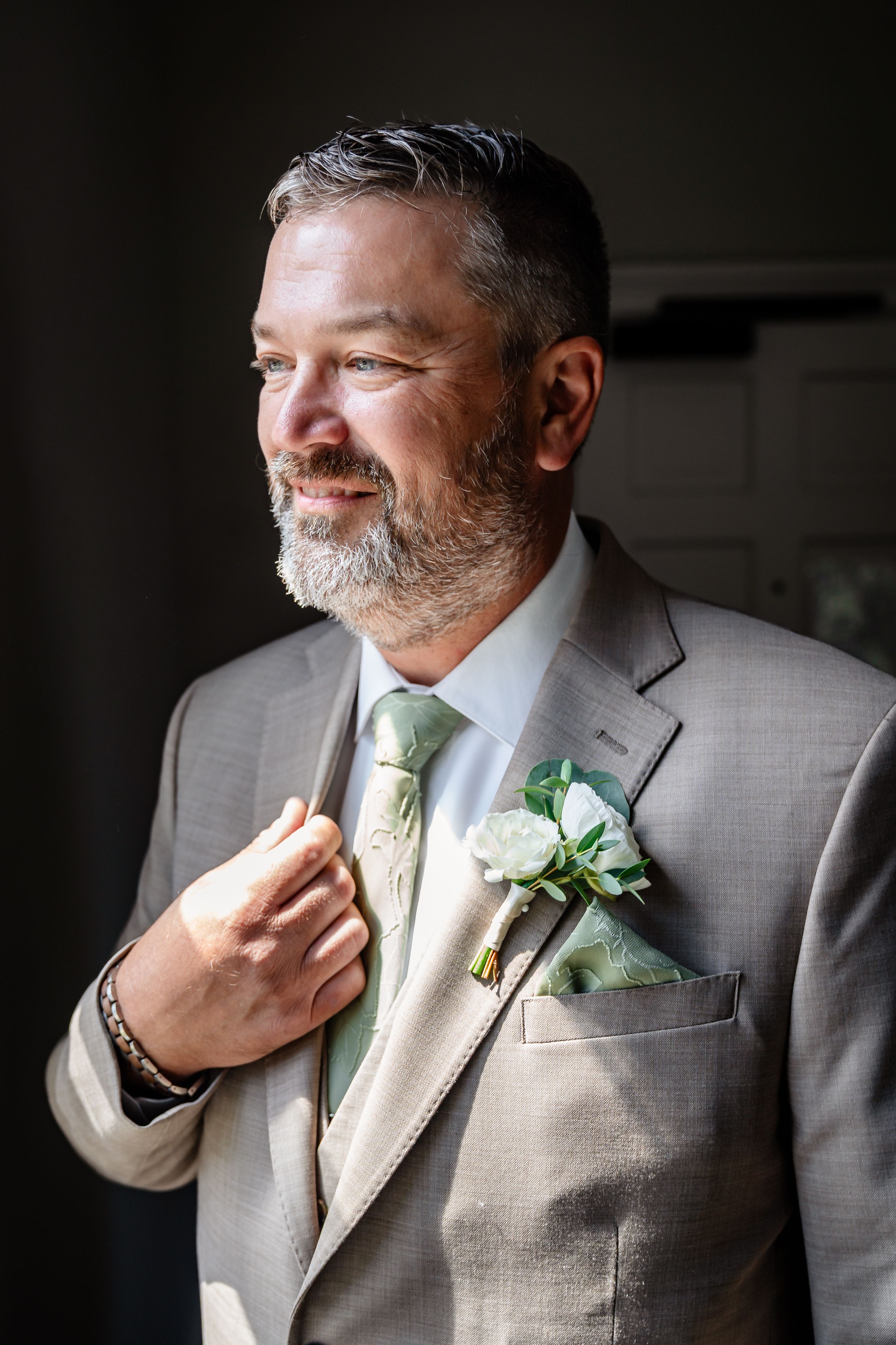 Smiling groom in gray suit with white boutonniere and green tie.