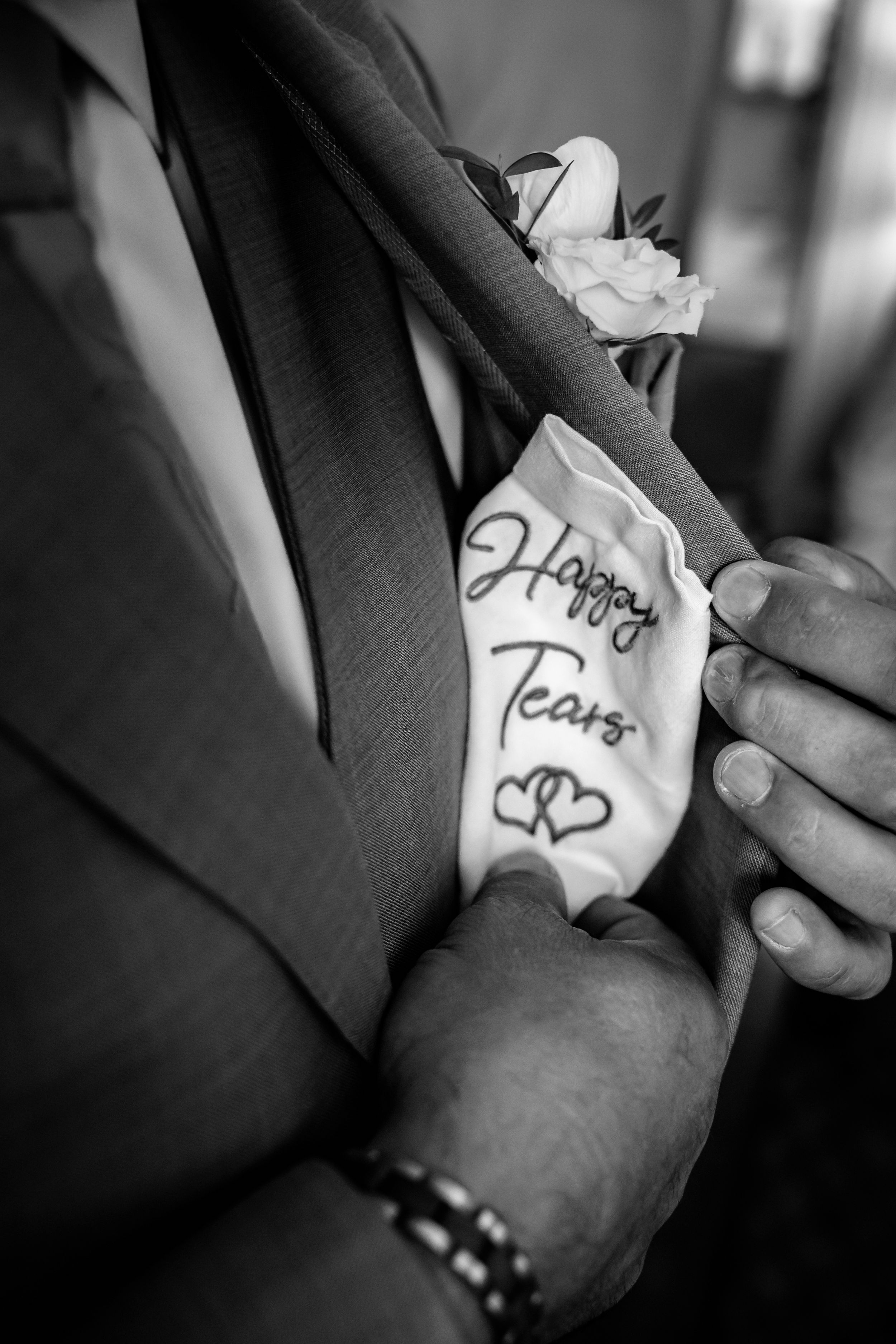 Black and white photo of groom holding a handkerchief embroidered with Happy Tears and hearts on wedding day.