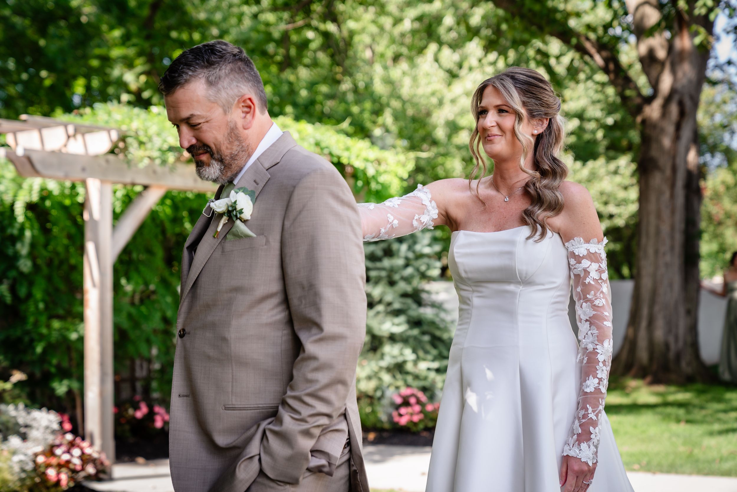 Emotional groom reacts during outdoor wedding first look with smiling bride in lace gown.