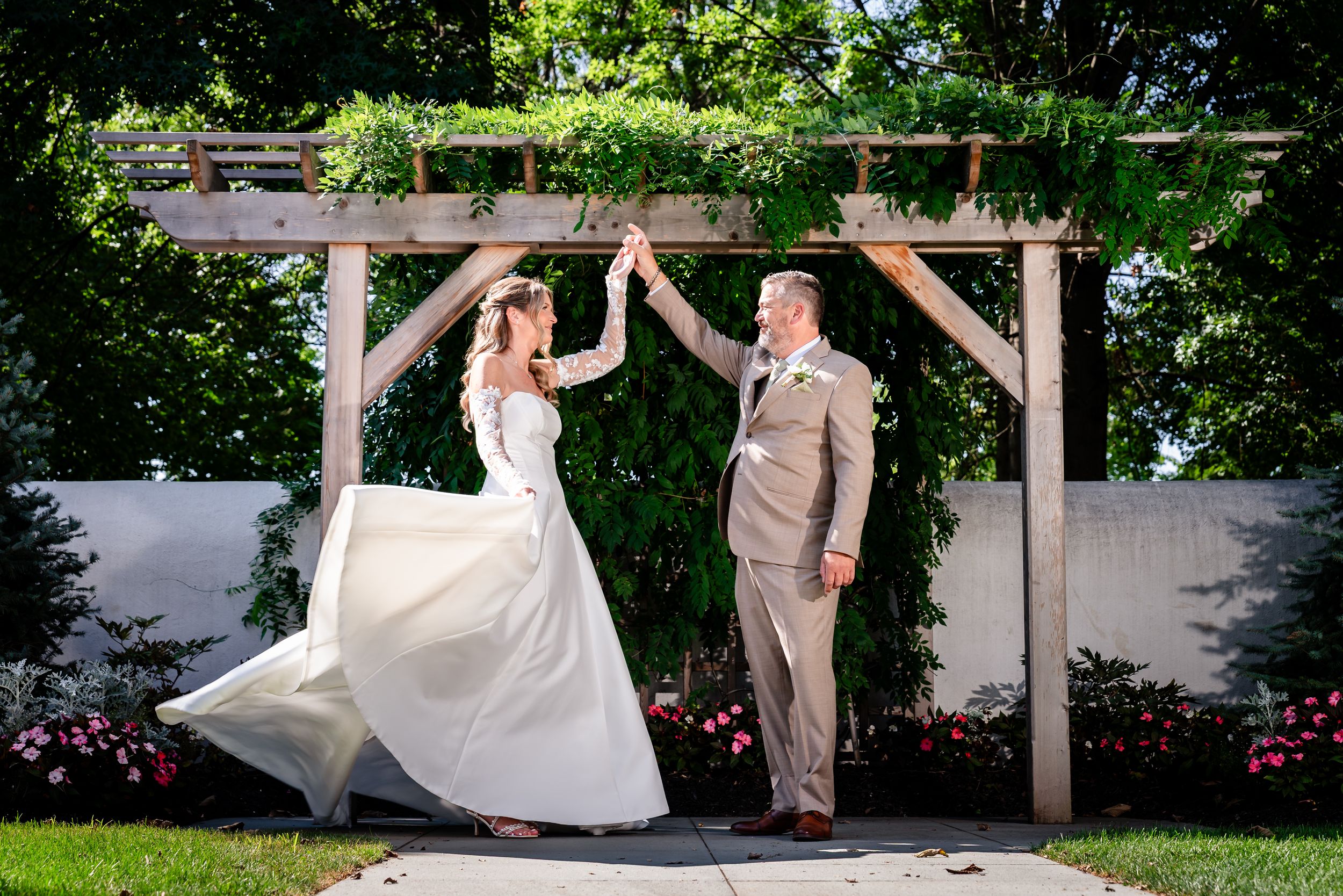 Bride and groom dancing under a wooden pergola with lush greenery at an outdoor wedding ceremony.
