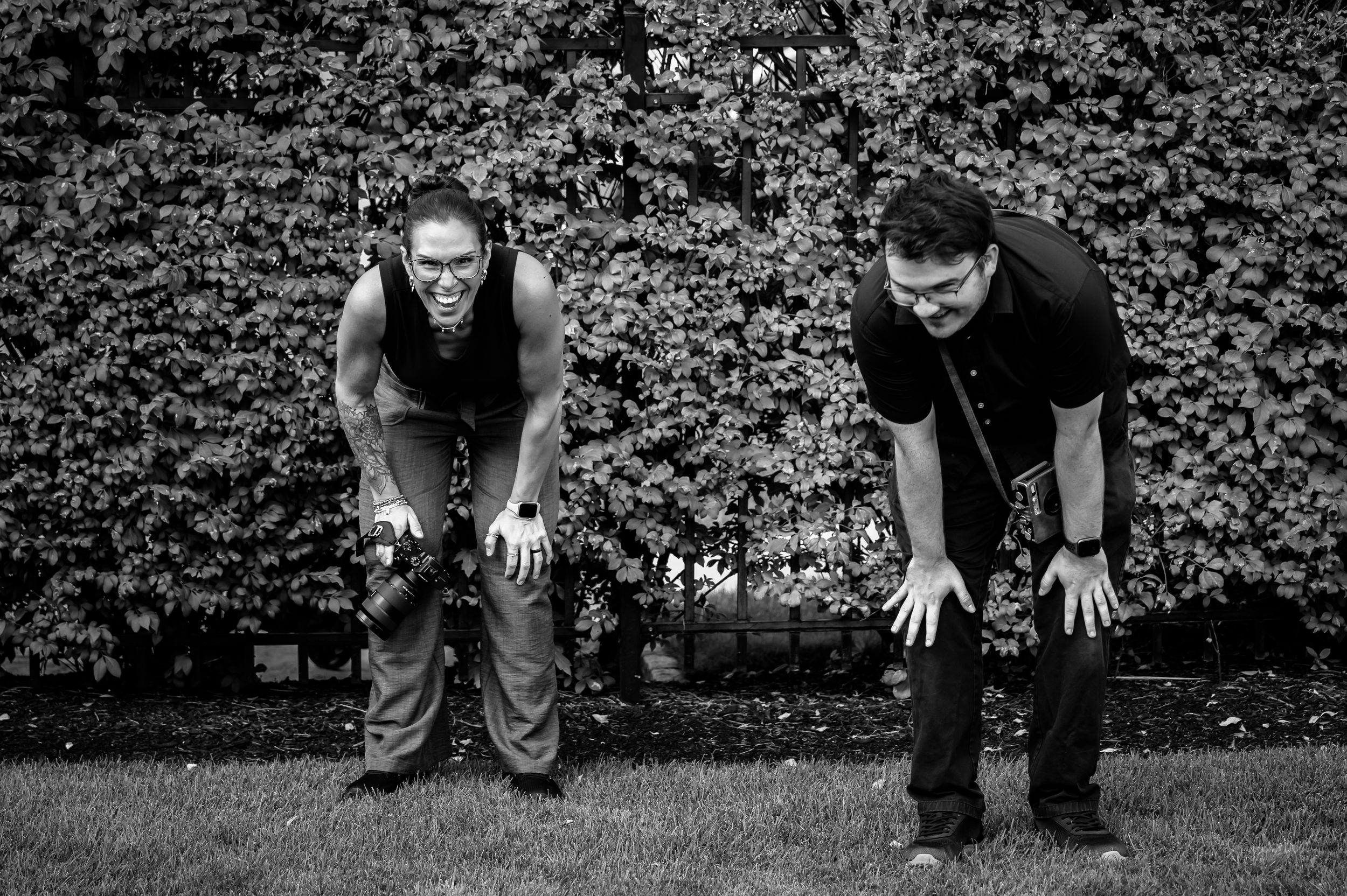 Two wedding photographers crouching with cameras in black and white outdoor photo.
