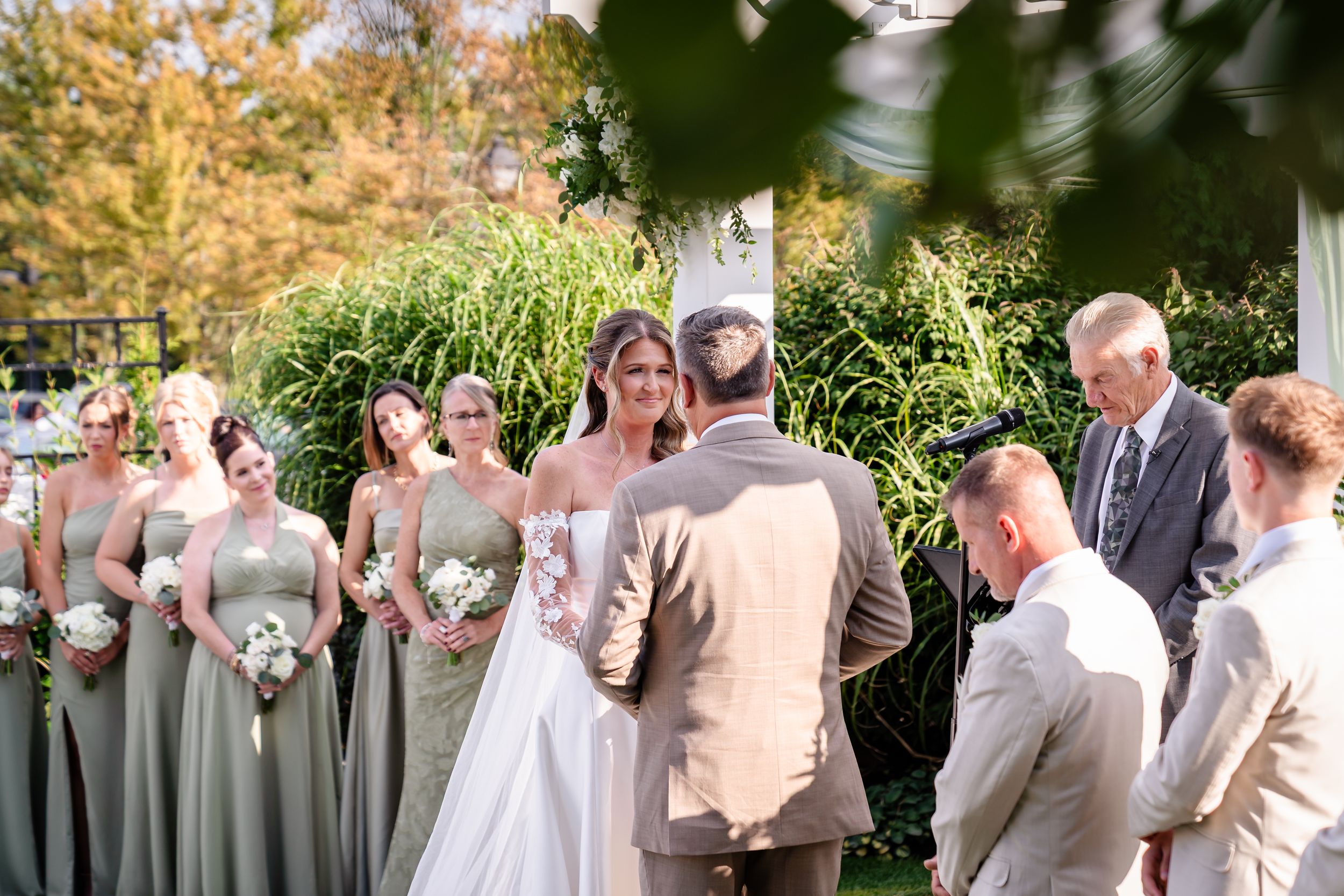 Bride and groom exchange vows at outdoor garden ceremony with sage green bridesmaids.
