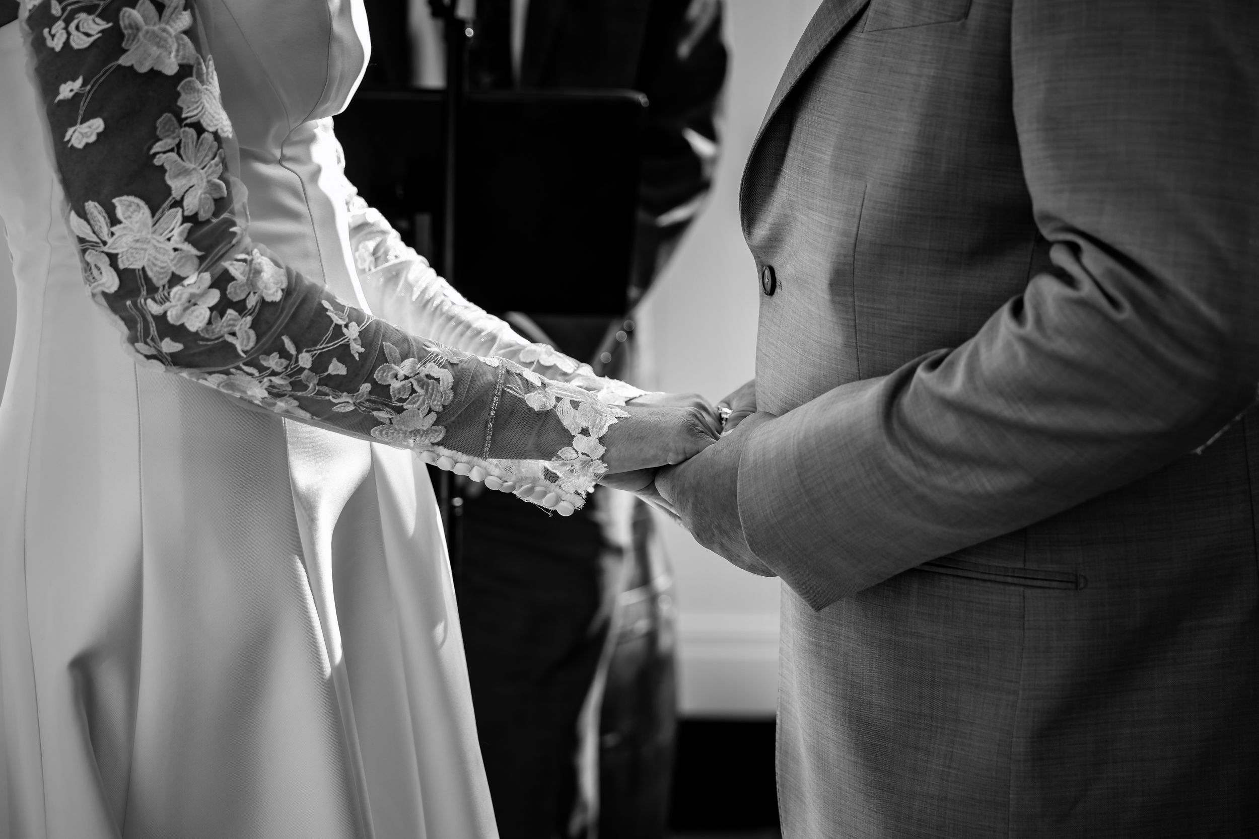 Black and white close-up of bride and groom holding hands during wedding ceremony at the altar.