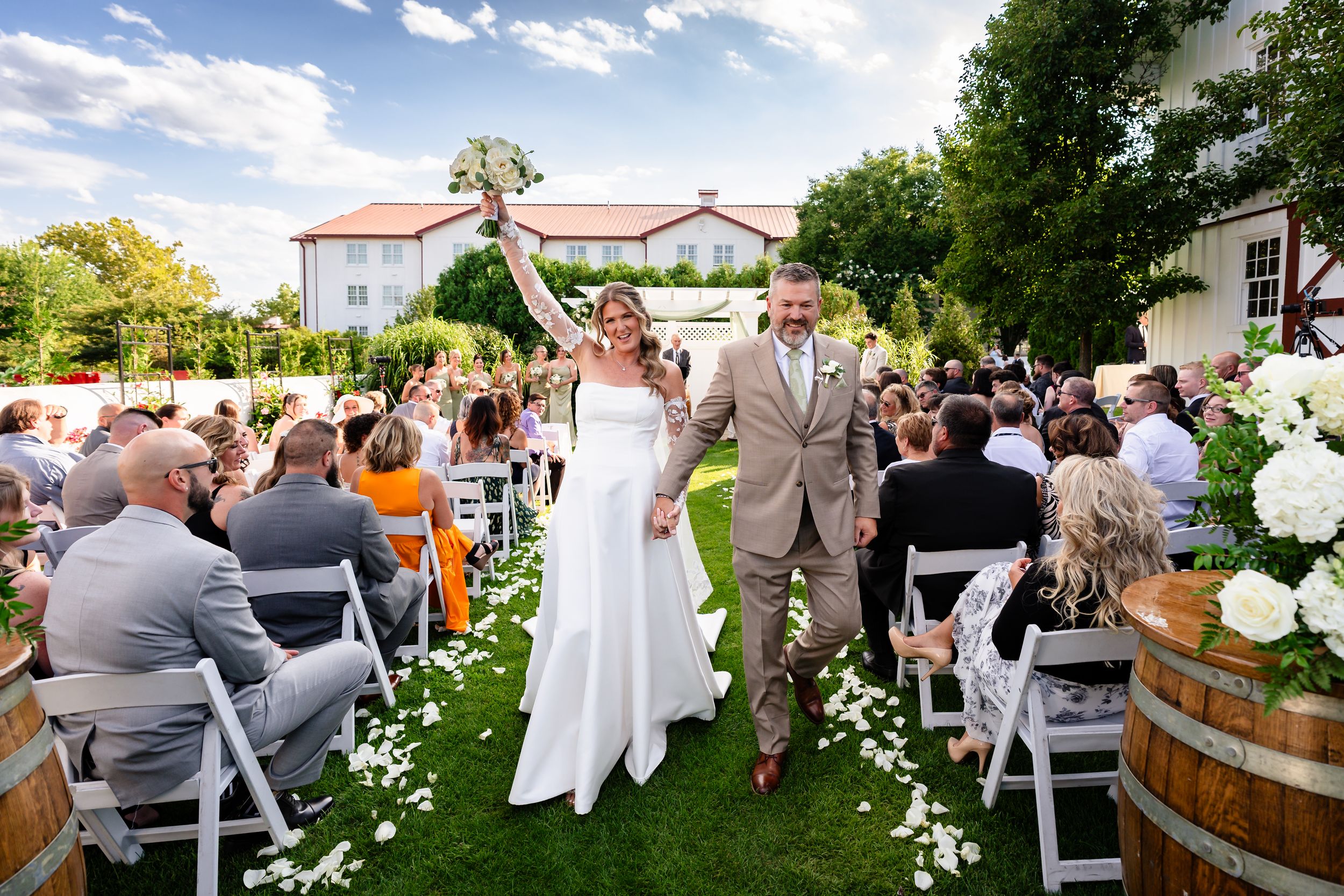 Joyful bride and groom walk back down the aisle after outdoor wedding ceremony at elegant vineyard venue.