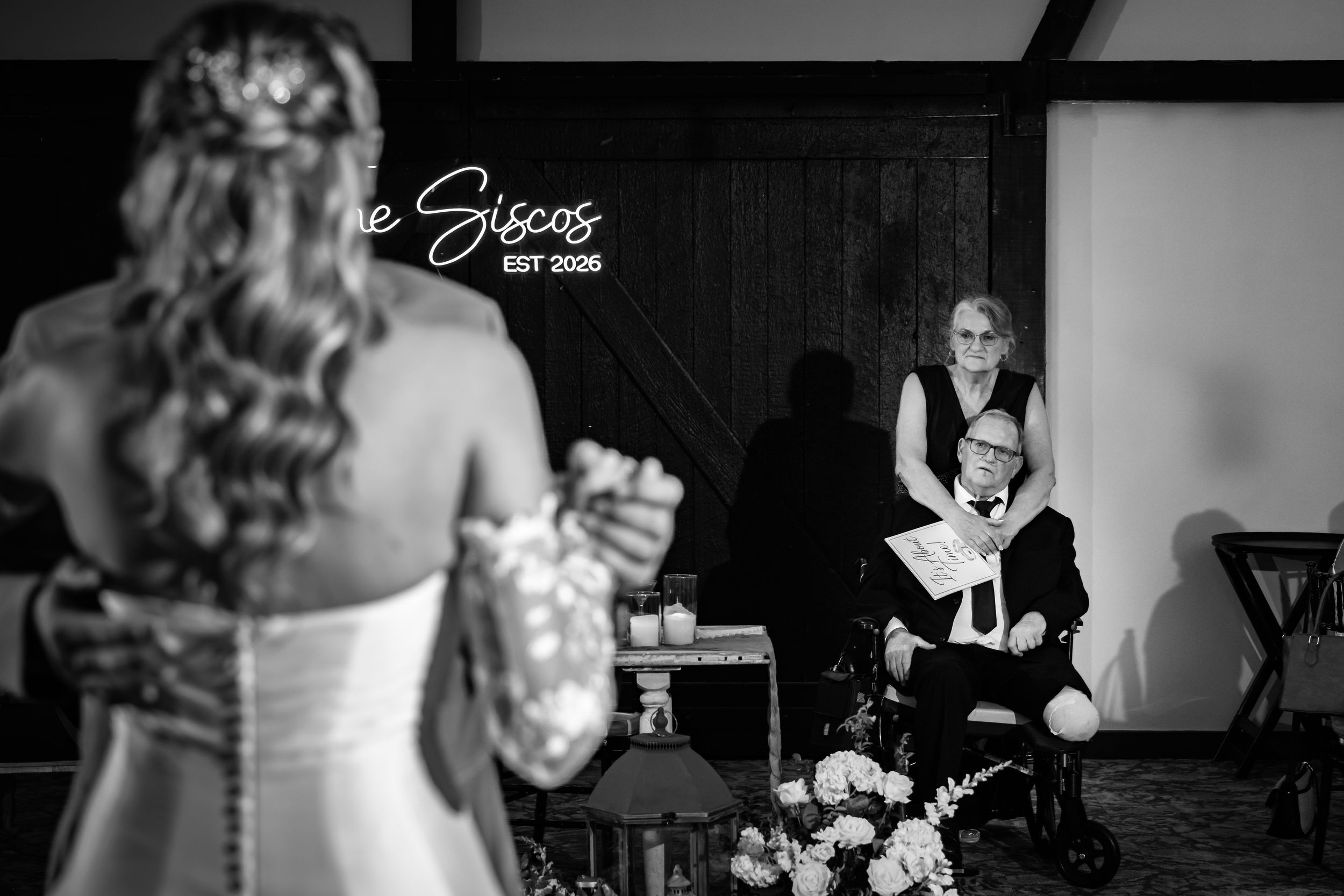 Black and white wedding photo of bride facing groom on one knee, with officiant smiling in background.
