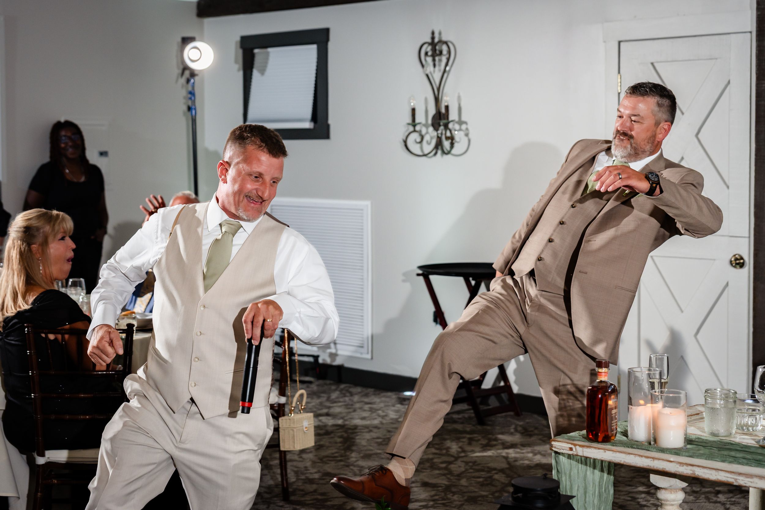 Two men in suits dancing and celebrating at a wedding reception indoor venue.
