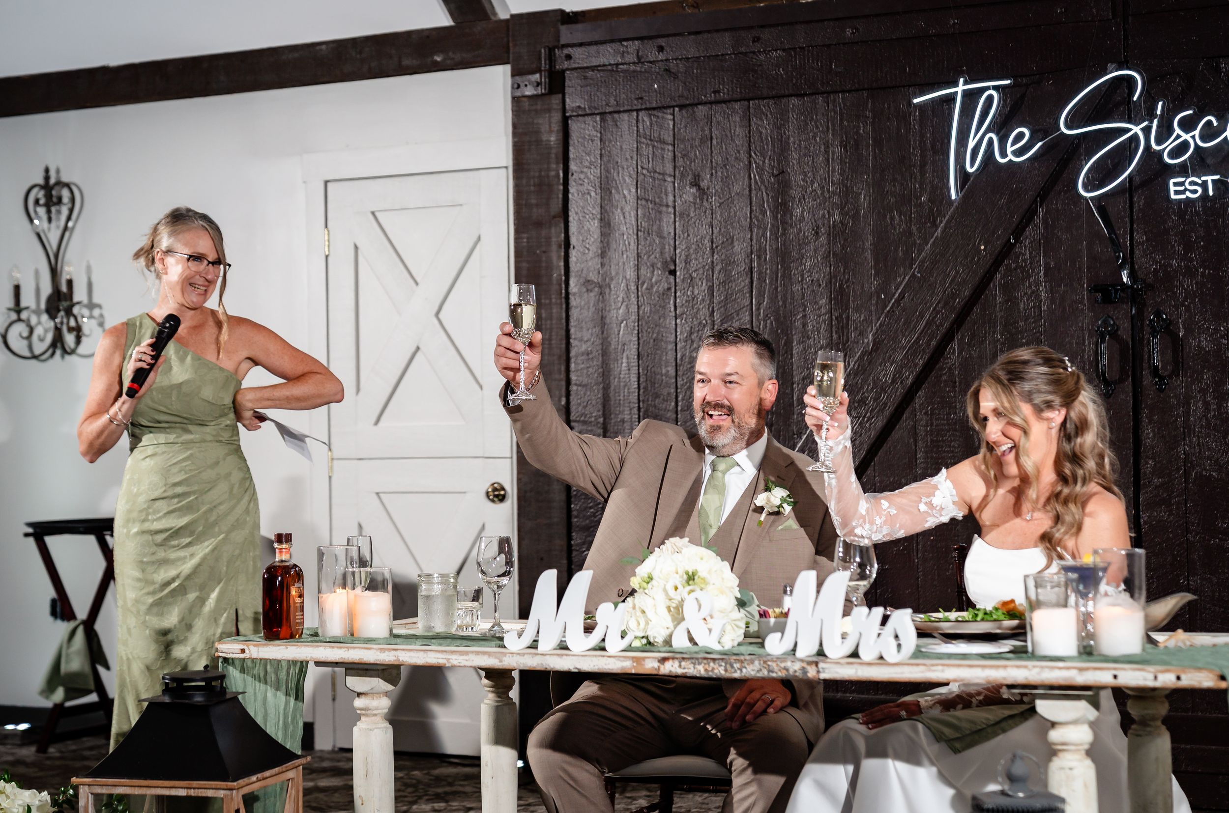 Bride and groom raise champagne glasses during wedding toast at sweetheart table with Mr and Mrs letters.