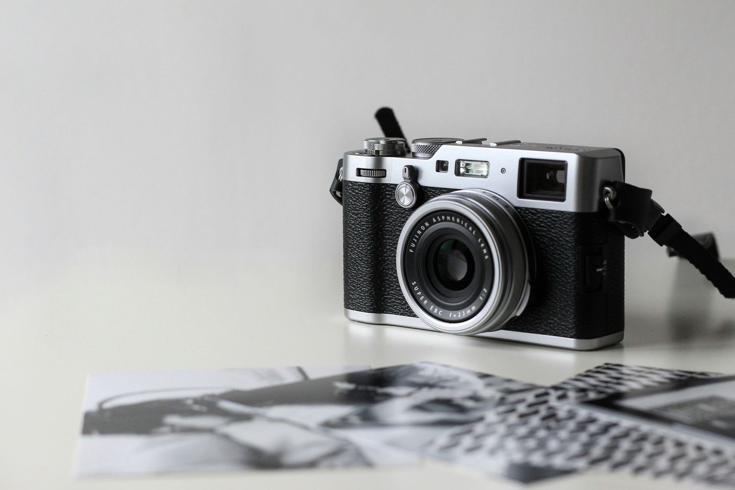 Vintage-style Fujifilm X100 compact camera resting on black and white photographs on a white surface.