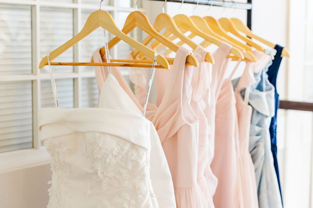 White wedding gown and pastel bridesmaid dresses hanging on wooden hangers on a clothing rack.