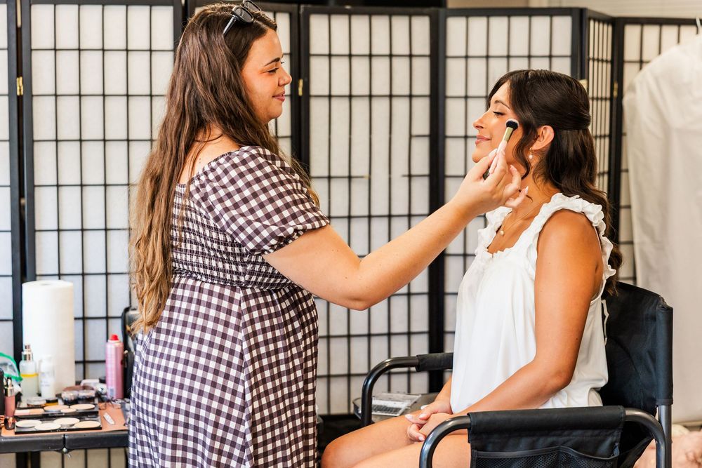 Makeup artist applying foundation to a seated bride during wedding day preparations indoors.