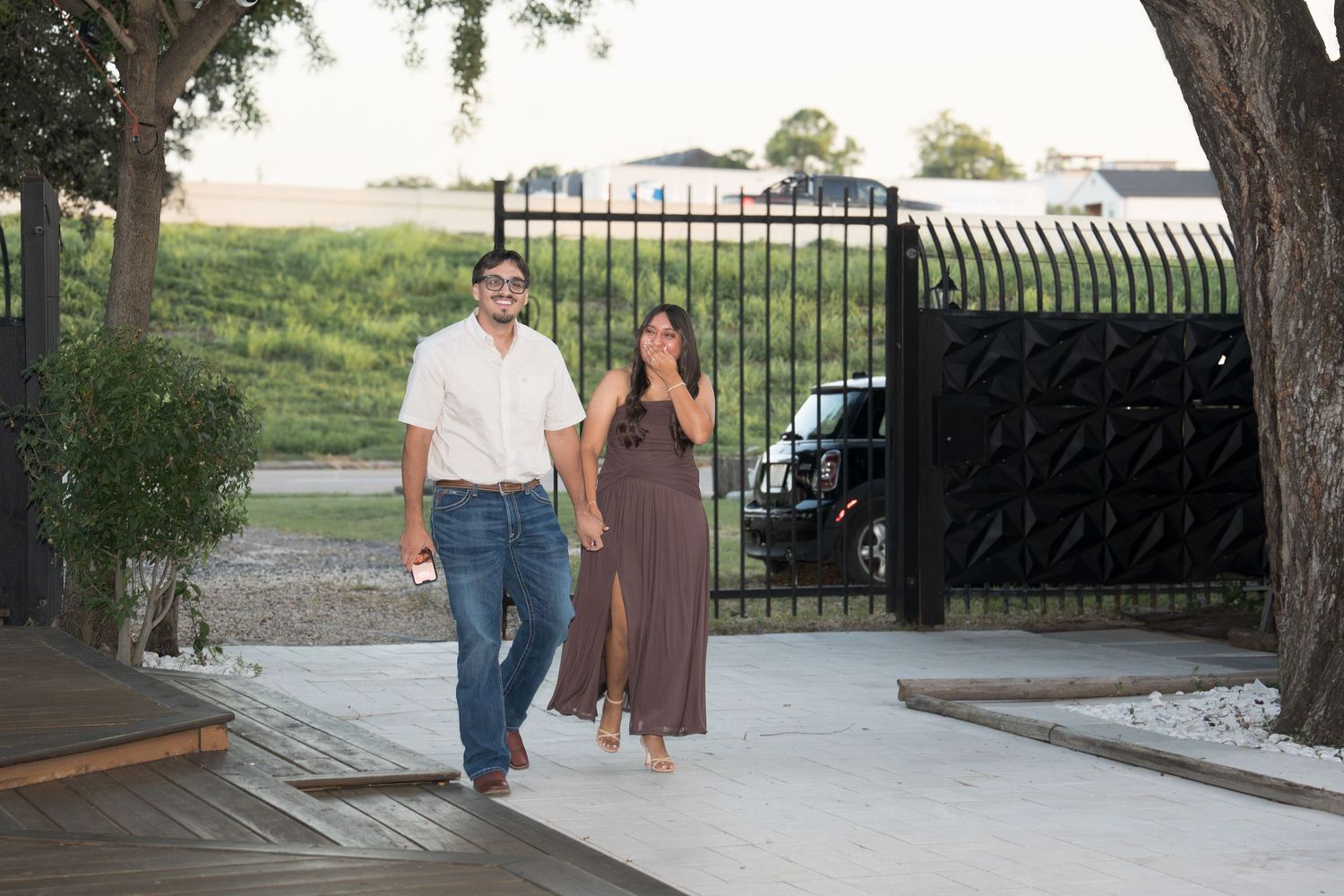 Couple walking hand in hand through elegant black iron gate at outdoor venue.
