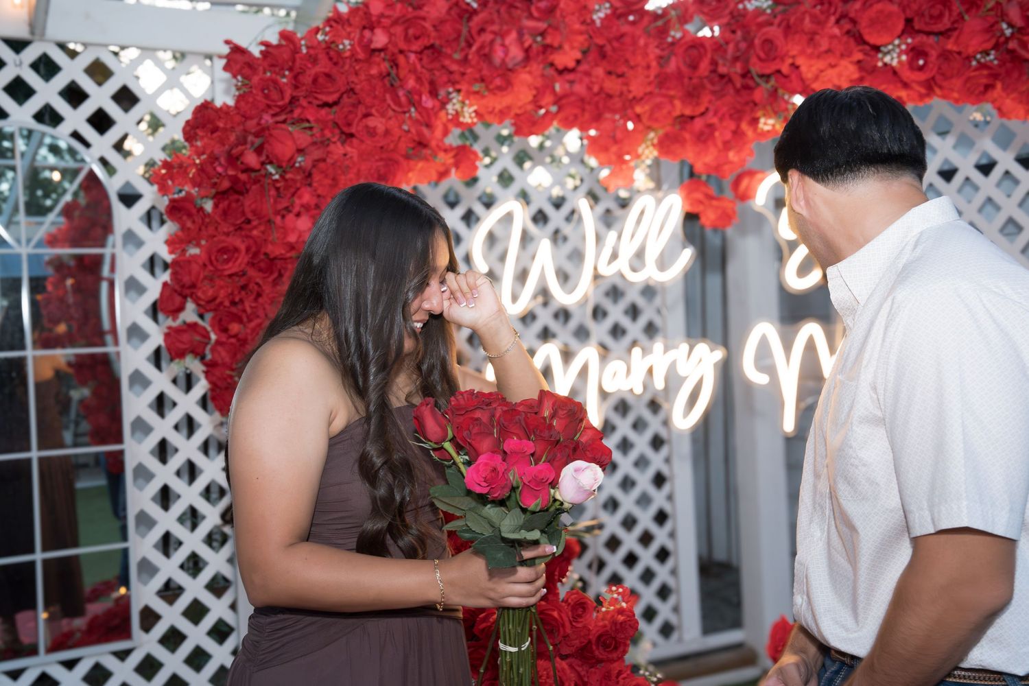 Romantic marriage proposal with red roses and Will You Marry Me neon sign backdrop.