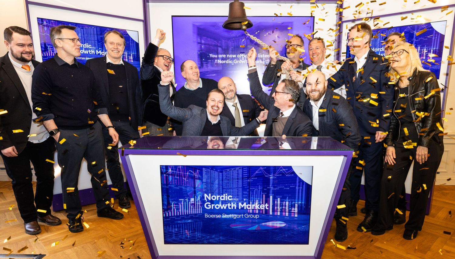 Group of professionals celebrating at Nordic Growth Market podium with confetti and bell-ringing ceremony.