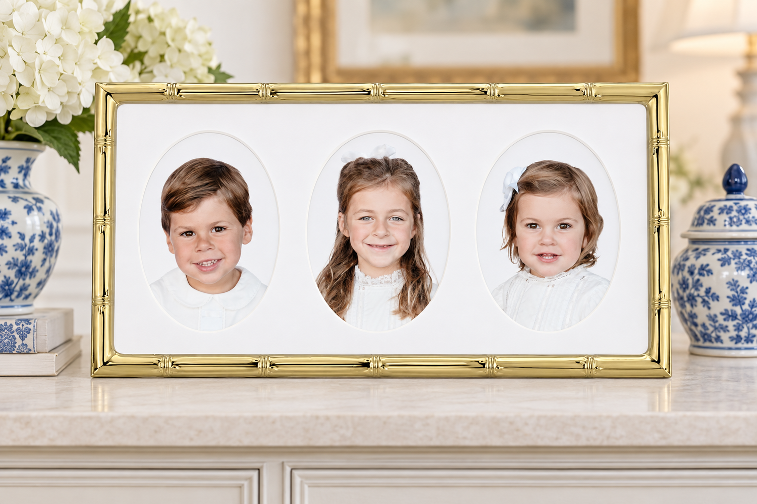 Gold bamboo triple photo frame displaying portraits of three children on a white mantel with blue and white vases.