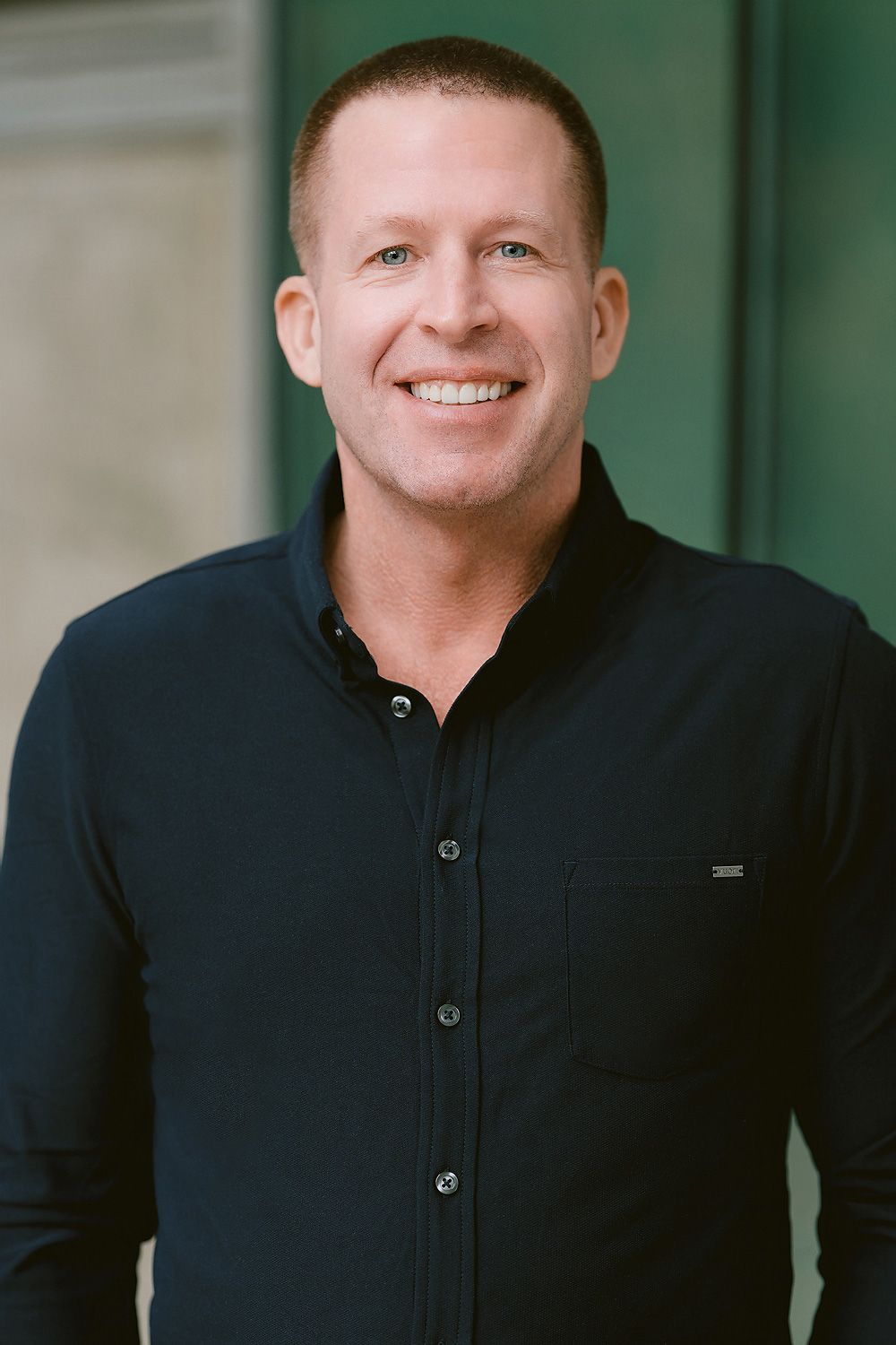 Smiling man in black shirt poses outdoors for professional headshot photo.