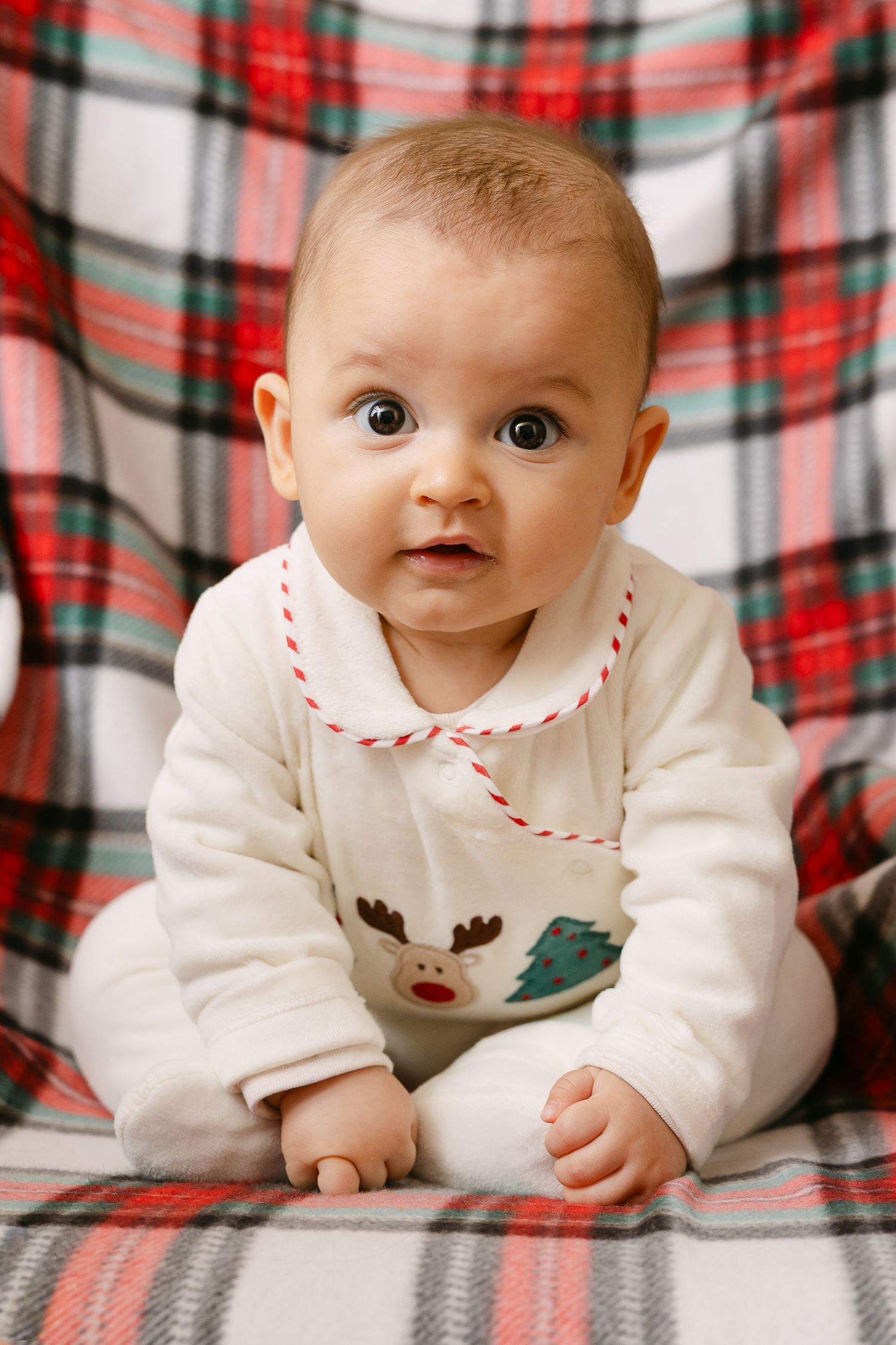 Child in red plaid outfit sits on beige couch near Christmas decorations.