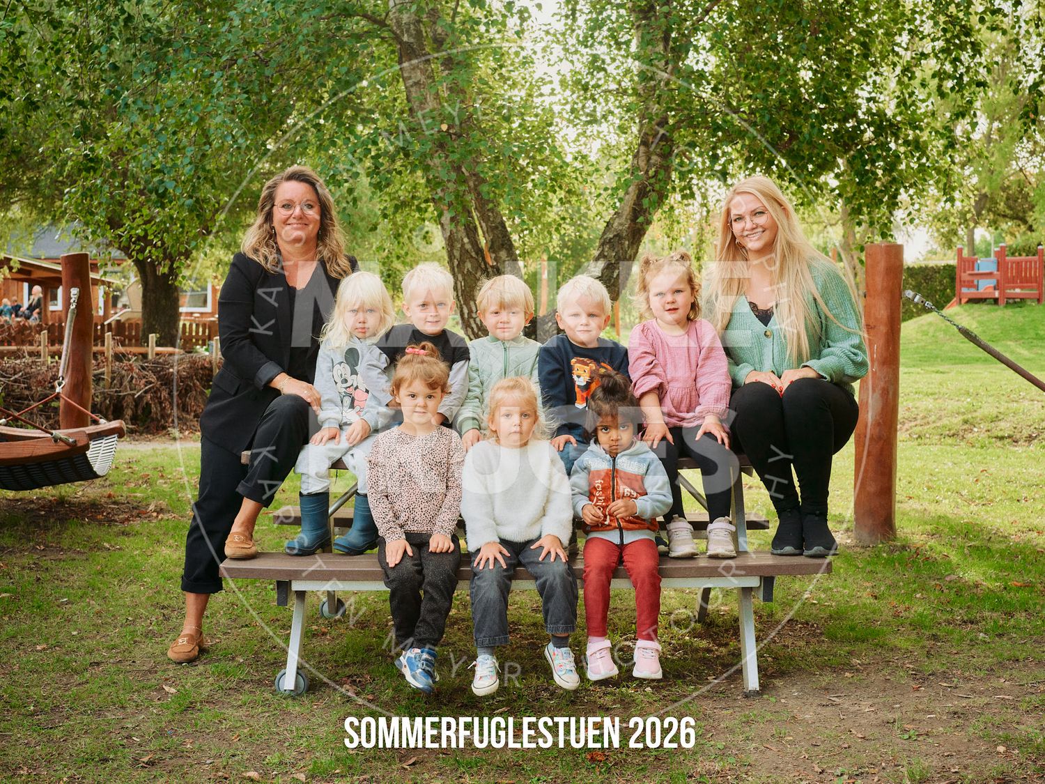 Group photo of children and two teachers at Brumbassestuen 2026 kindergarten, posing outdoors on a bench.