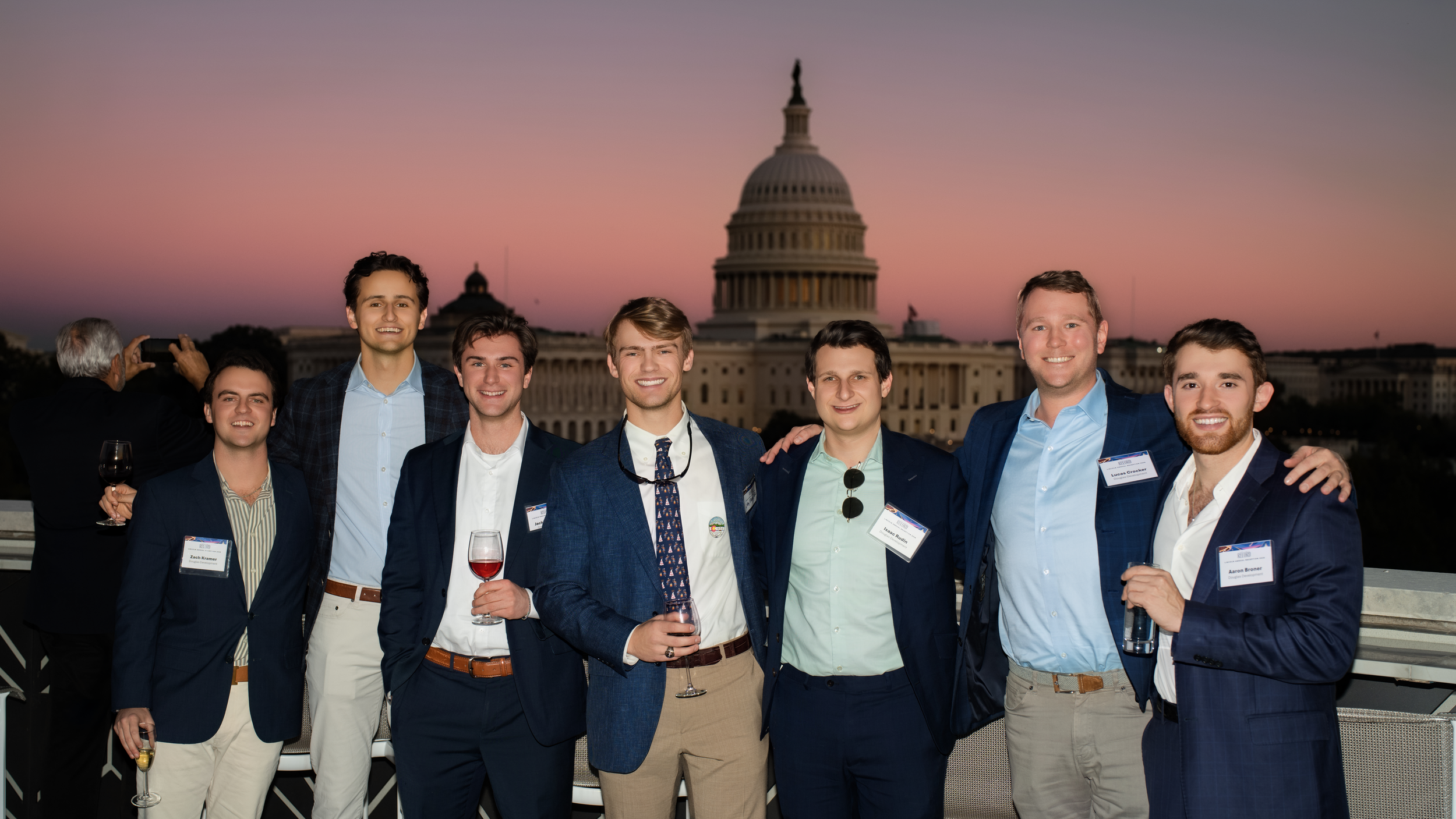 Seven guests pose on the 101 Constitution rooftop at twilight with the U.S. Capitol behind them.