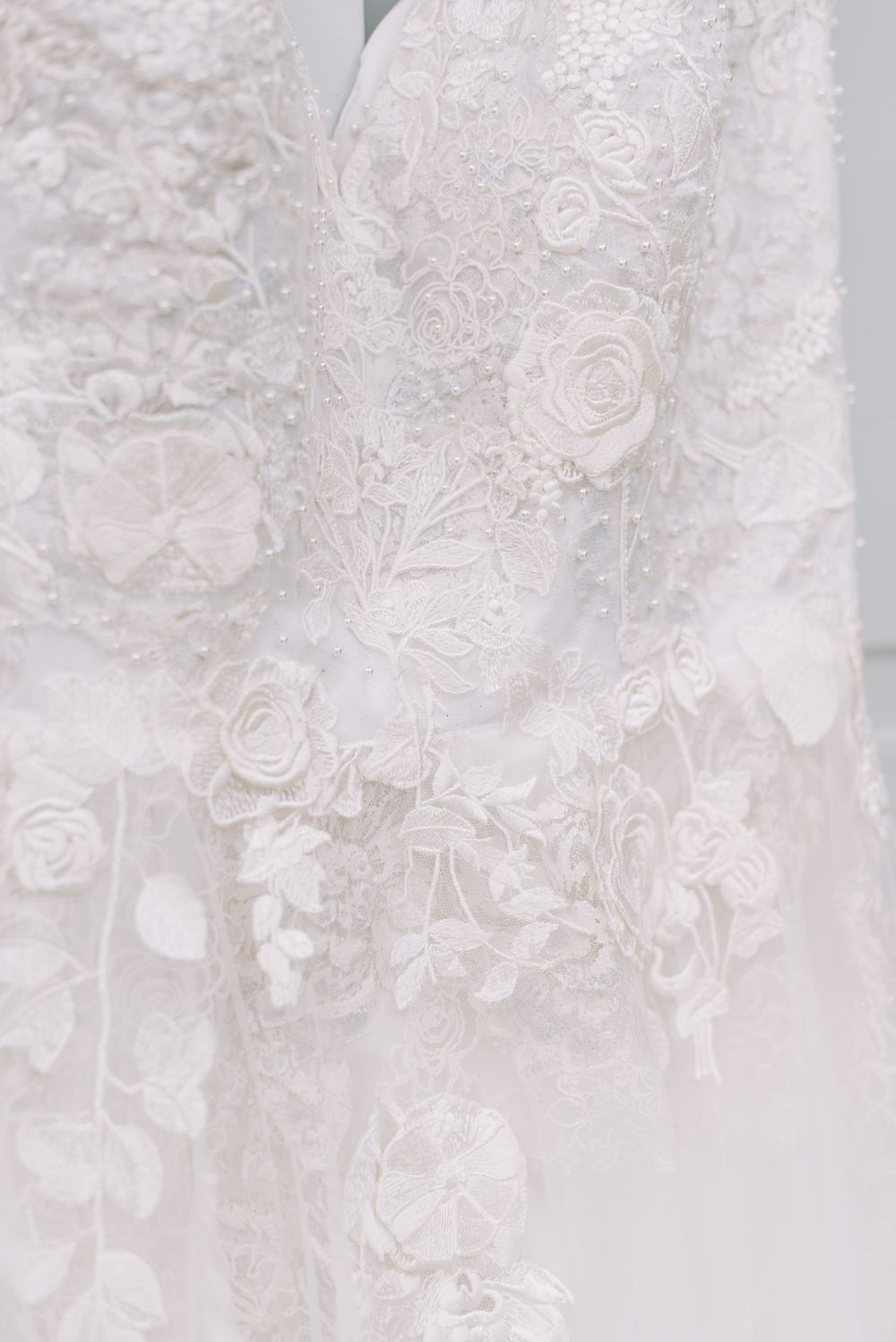 Close-up of an ivory wedding dress with delicate 3D floral lace appliqués, beaded embroidery, and soft tulle detailing.