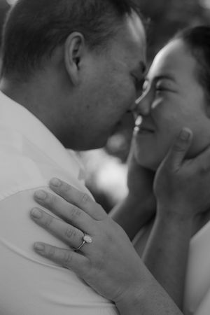 Black and white close-up of a couple nose to nose in a tender moment, her hand on his shoulder showing a sparkling engagement ring.
