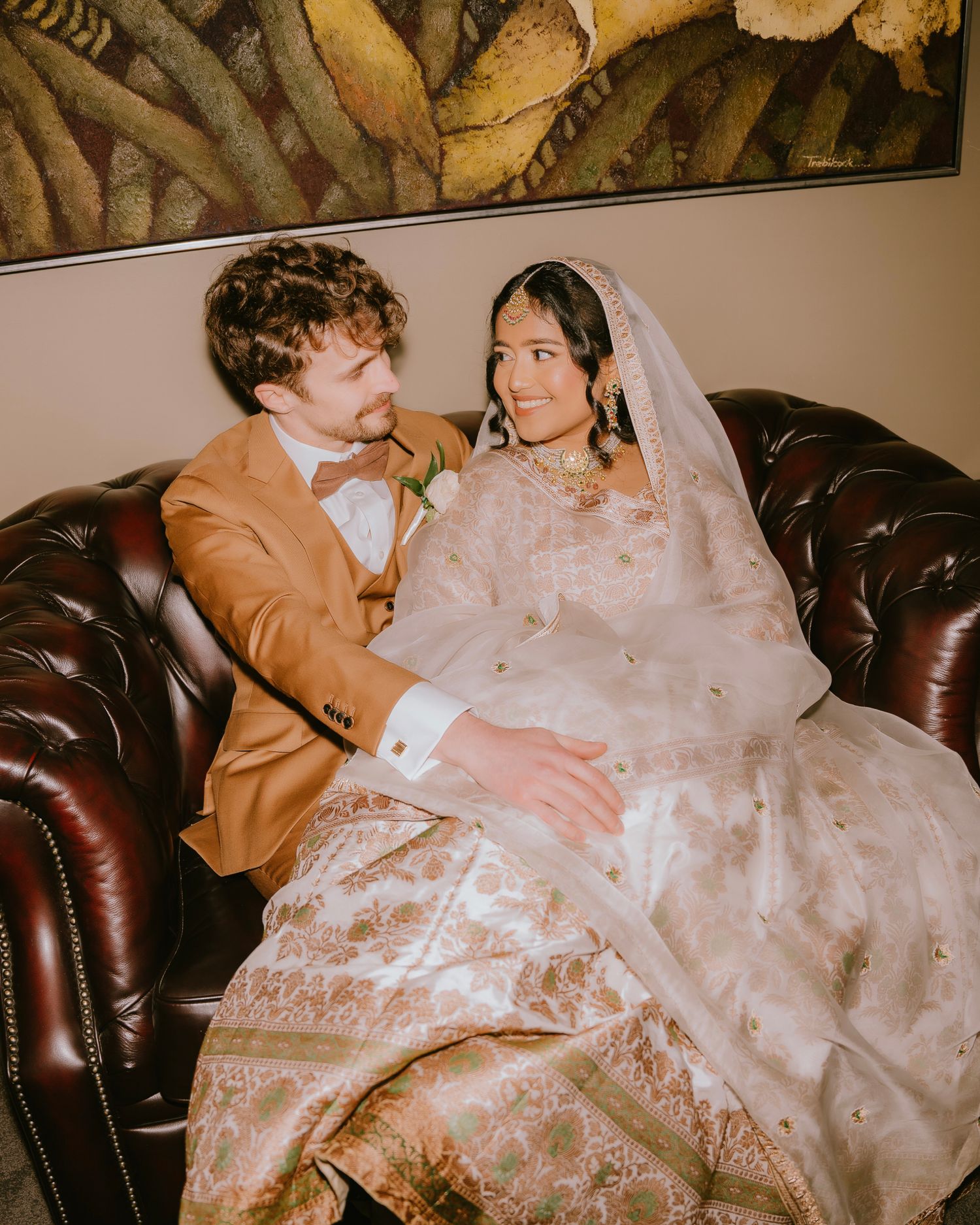 Bride in an ivory and gold embroidered lehenga beside her groom on a leather sofa - Adelaide Pakistani and Indian wedding
