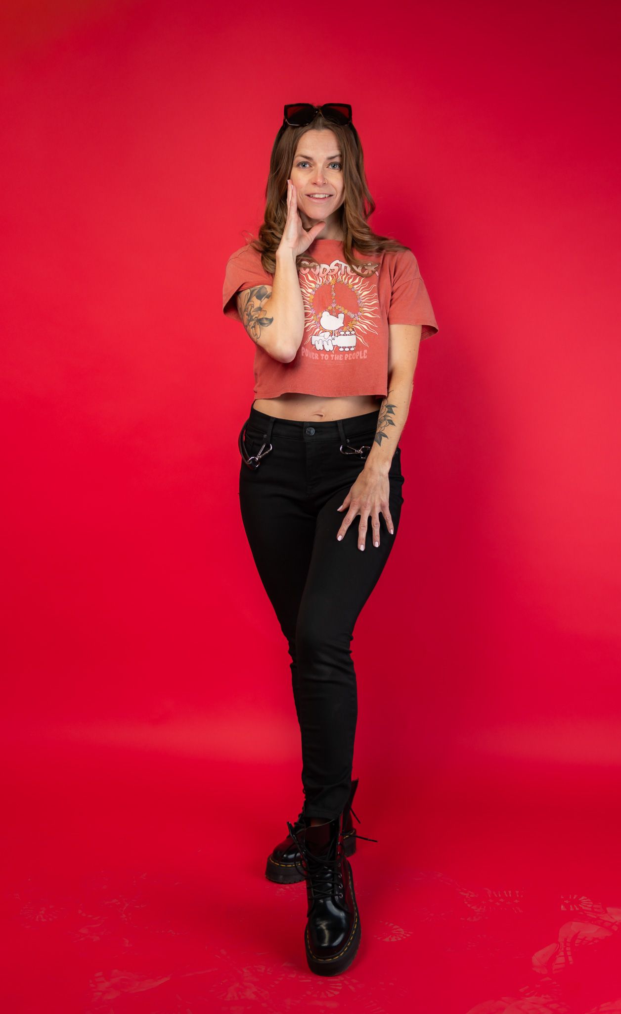 Full-length fashion portrait of Karly in a rust-colored top, black trousers and boots against a red studio background.