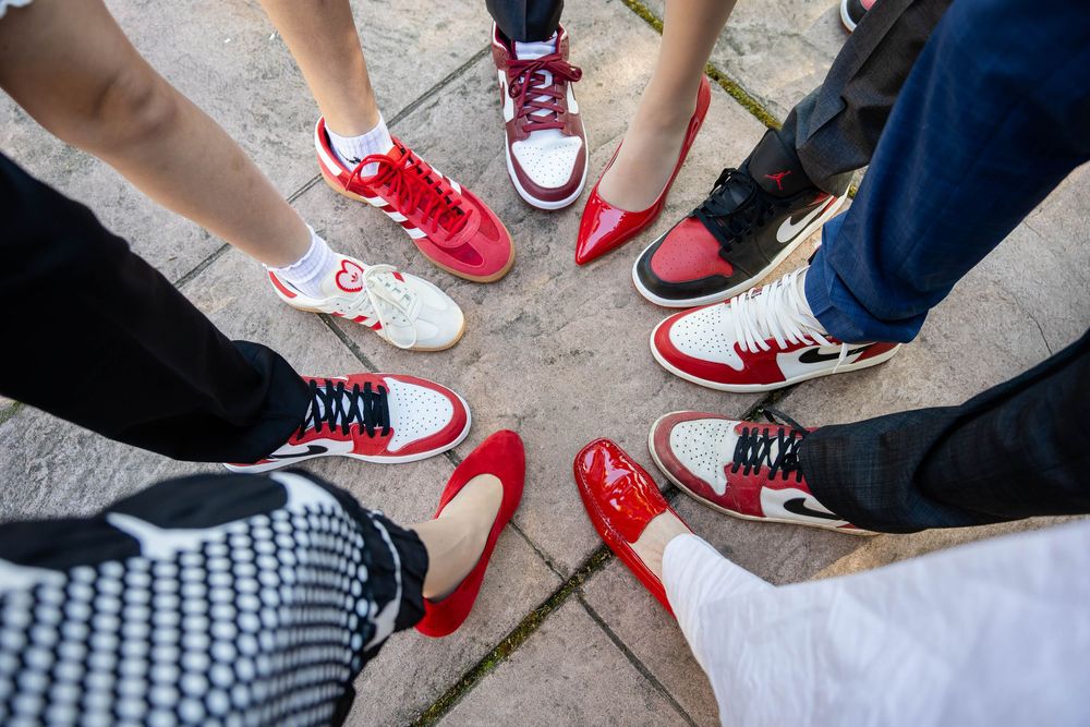 Overhead view of a circle of feet wearing red and white sneakers and red flats on a stone tile patio.