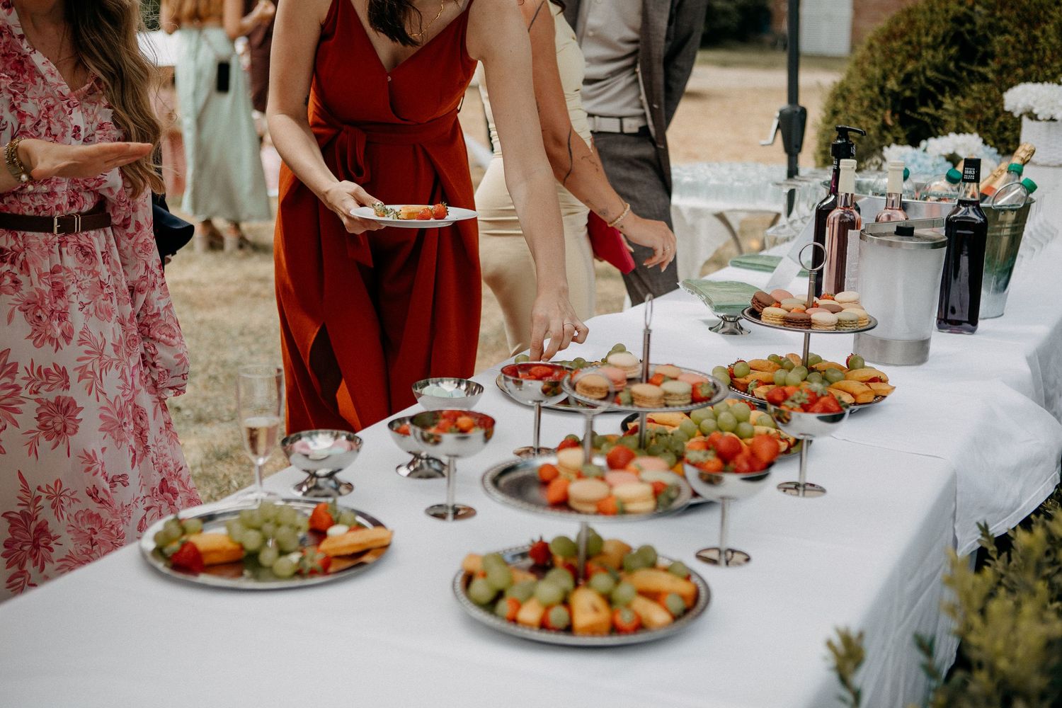 Guests serving themselves at an elegant outdoor buffet table with fruit platters and appetizers at a wedding reception.