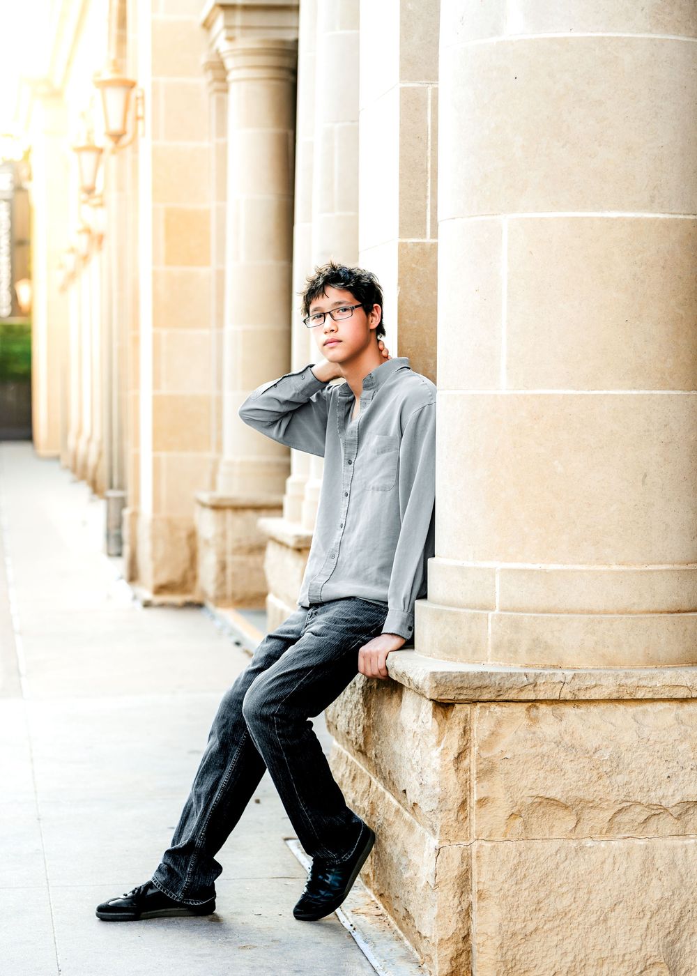 Young man in glasses and gray shirt leaning against stone column at a classic building.