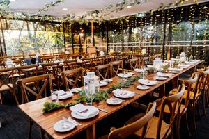 Elegant wedding reception venue with long wooden tables, greenery runners, white plates, and fairy lights overhead.