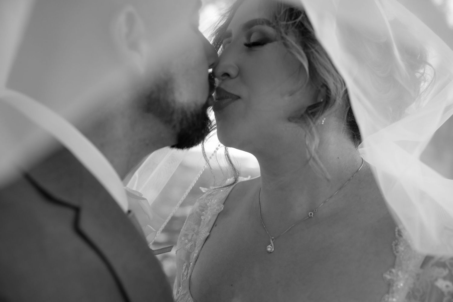 Two people share an intimate kiss with dramatic lighting and shadows in an emotional black and white photograph.