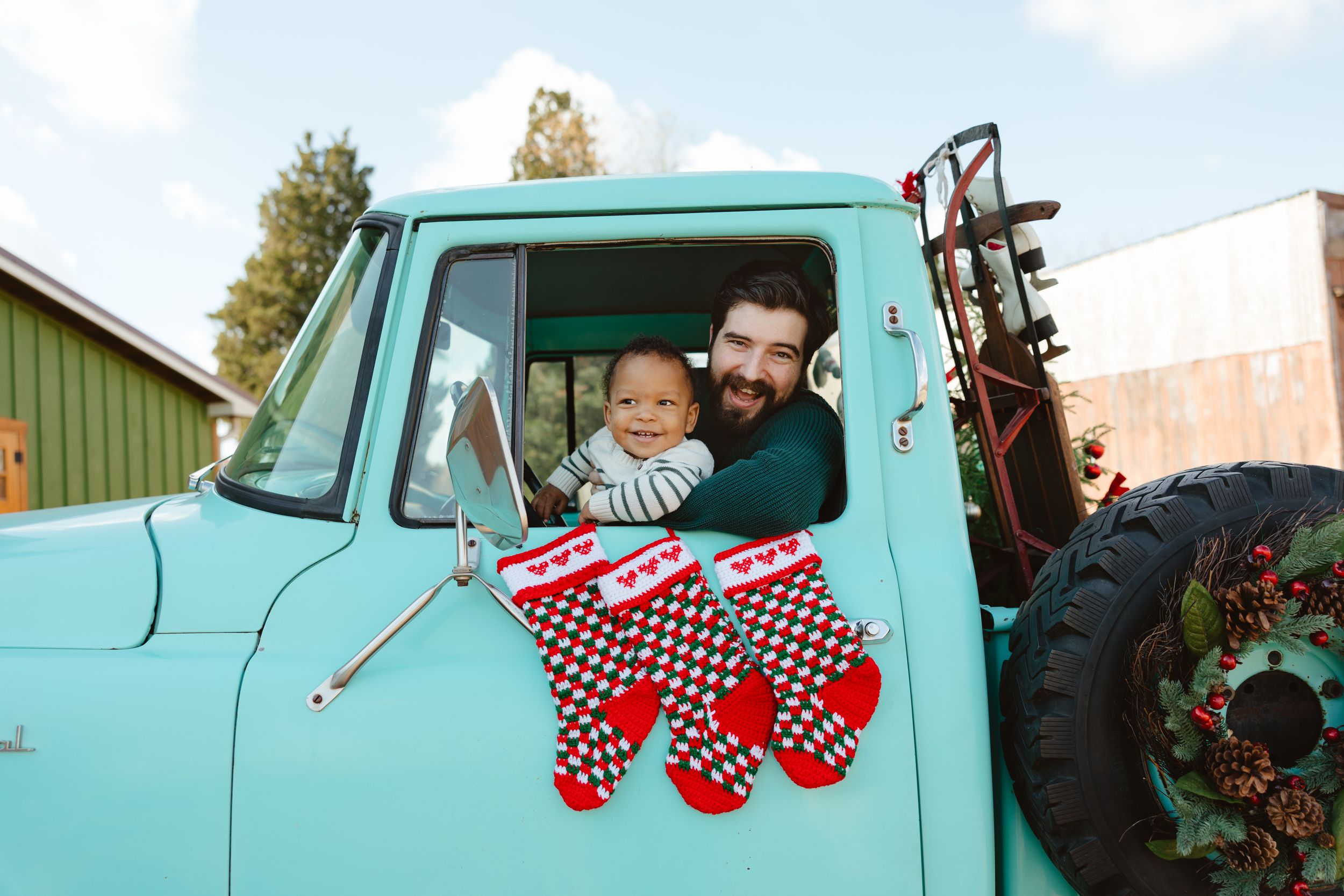 Man holding baby in vintage teal truck window with Christmas stockings hanging outside.
