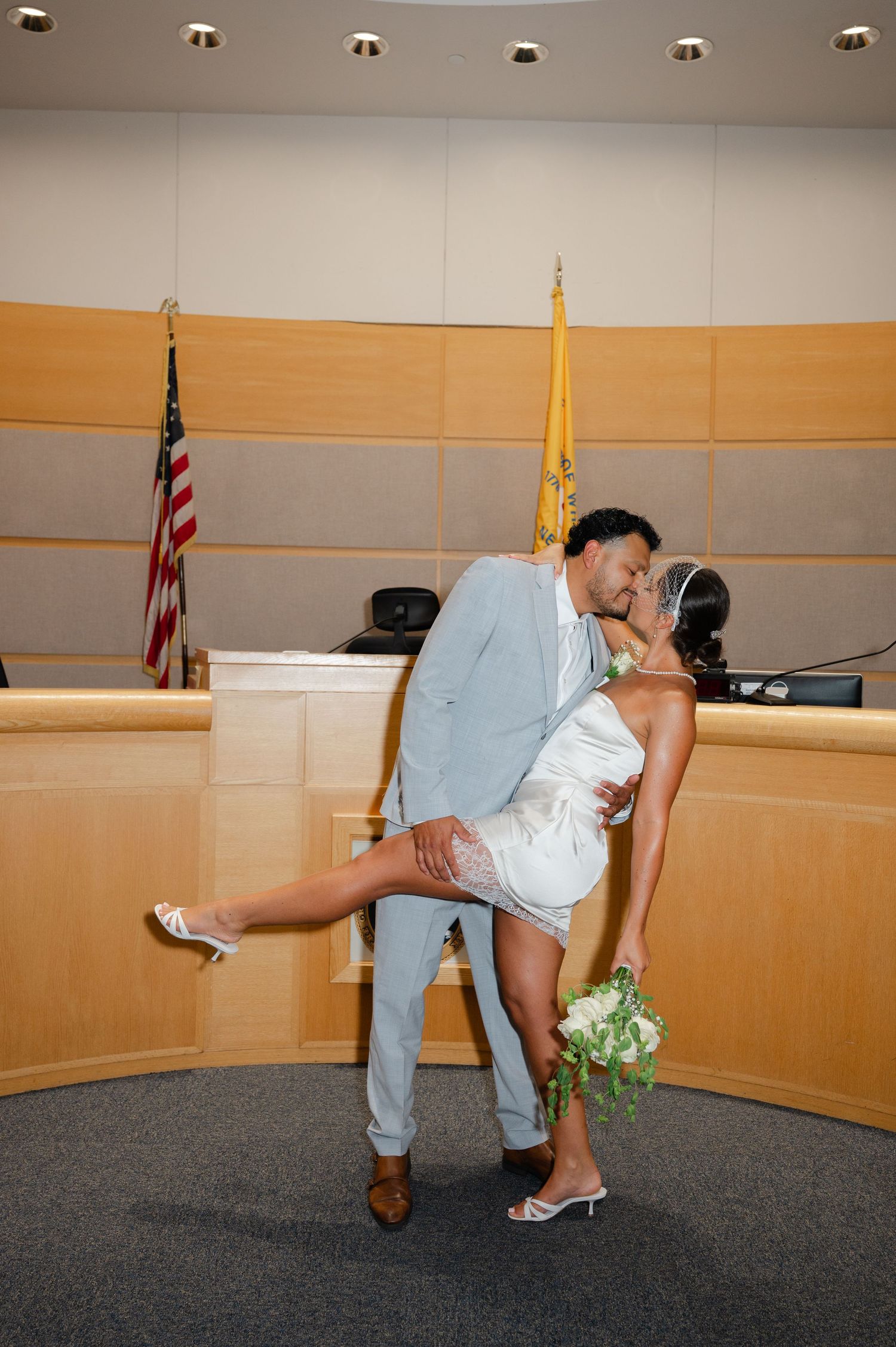 Couple sharing a romantic dip kiss after a courthouse wedding ceremony in Westchester, the bride in white mini dress holding bouquet.