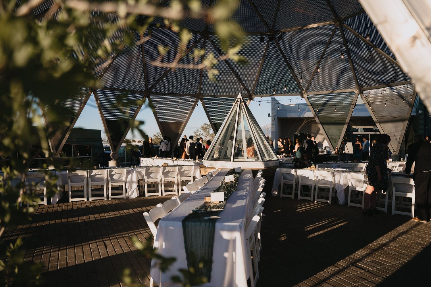 Modern building exterior with geodesic dome roof, yellow glass doors, circular windows, and white facade surrounded by trees.