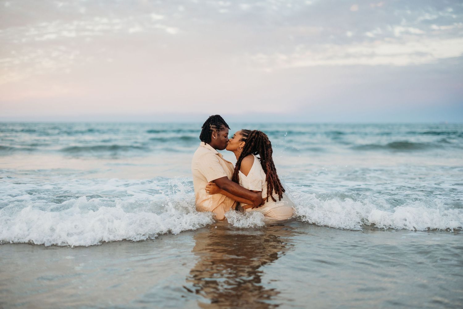 Couple kissing in ocean waves at sunset on a beautiful beach.