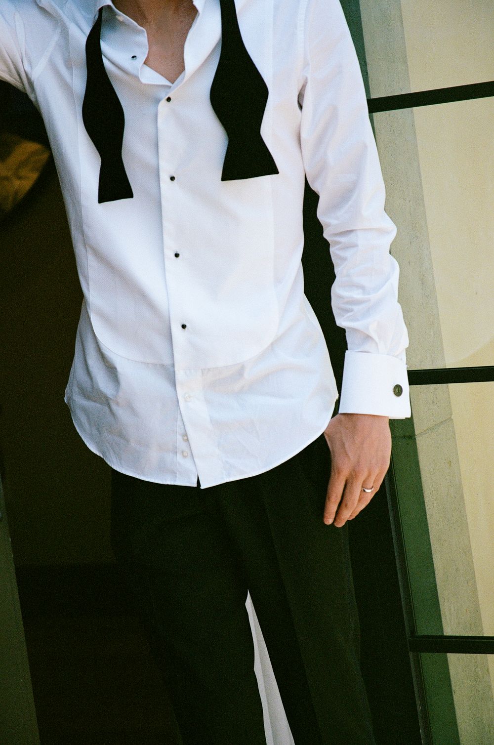Man in white tuxedo shirt with black bow tie and cufflinks, formal wedding attire closeup.