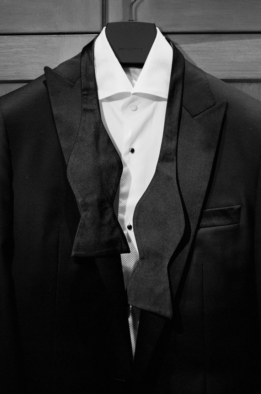 Black and white photo of a classic tuxedo with bow tie and white dress shirt on a hanger.