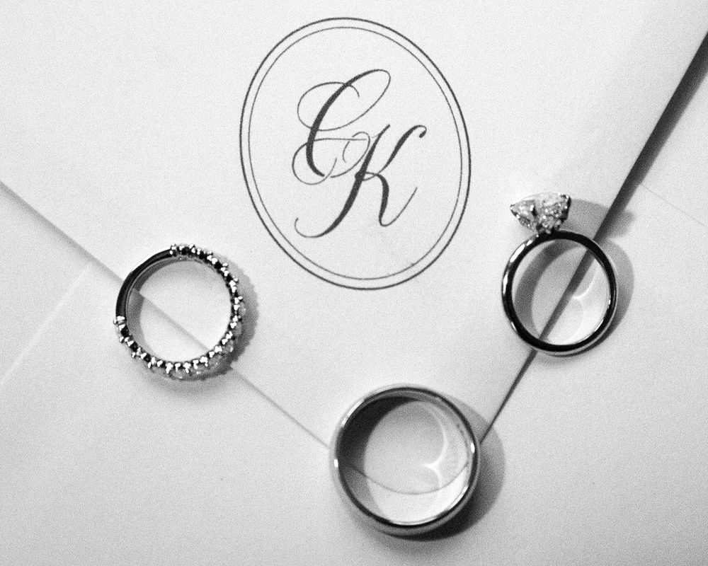 Black and white photo of wedding rings and engagement ring on monogrammed envelope with elegant CK initials.