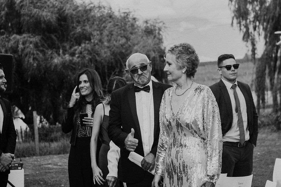Black and white photo of wedding guests gathered outdoors under willow trees.