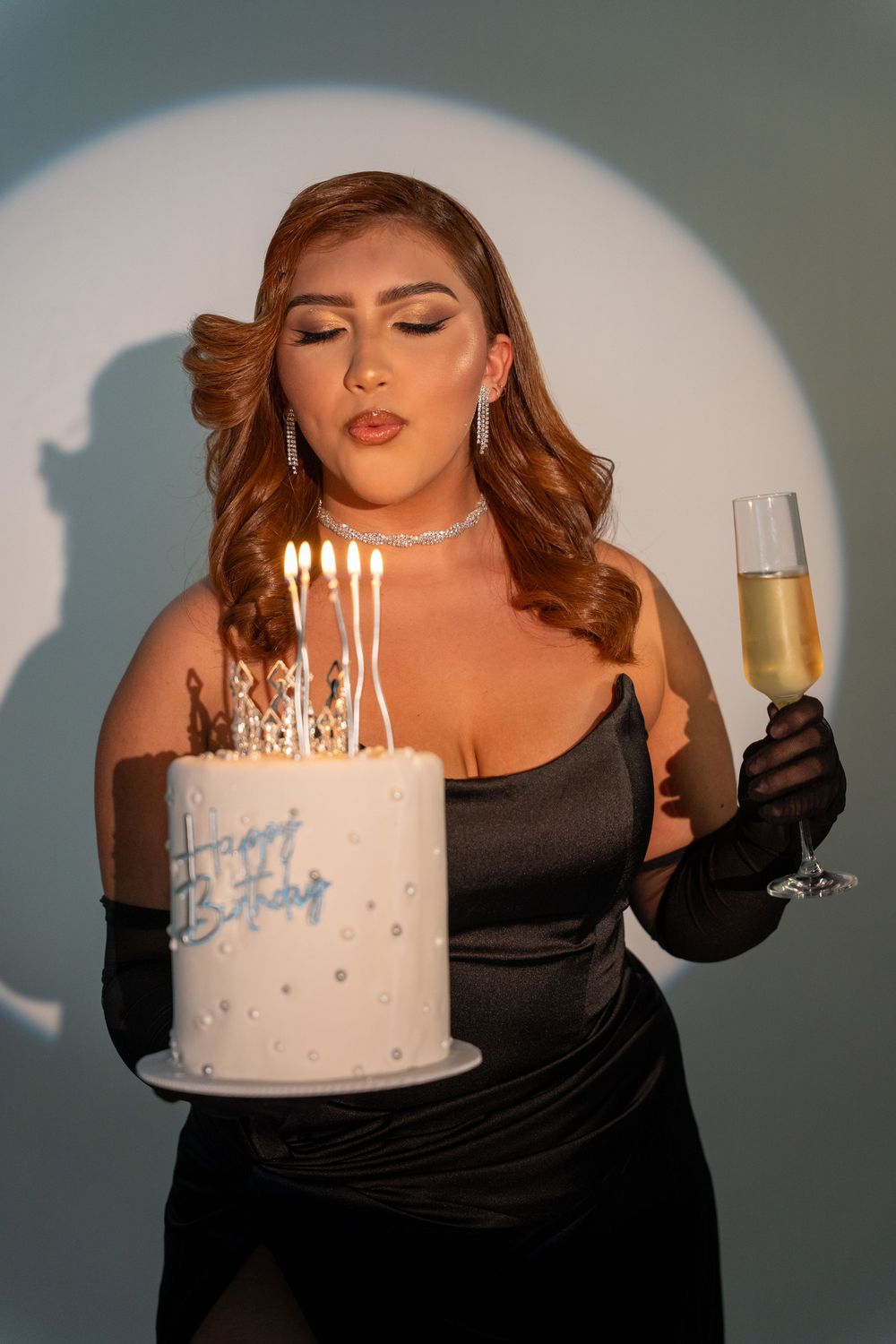 Woman blowing birthday candles during a creative studio portrait with spotlight lighting.